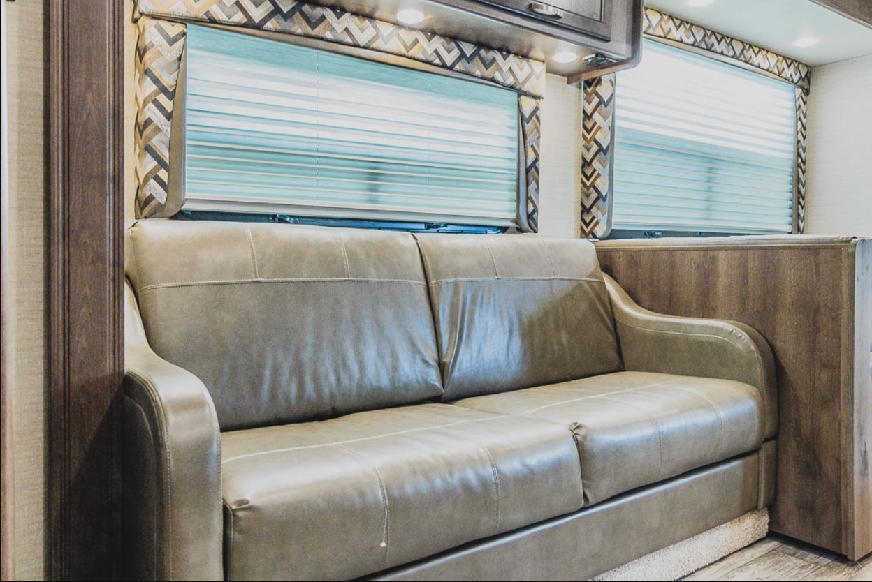 RV rental interior: A comfy leatherette sofa, two windows with blinds, and warm wood paneling create a cozy RV living space.. Jayco Redhawk 2018