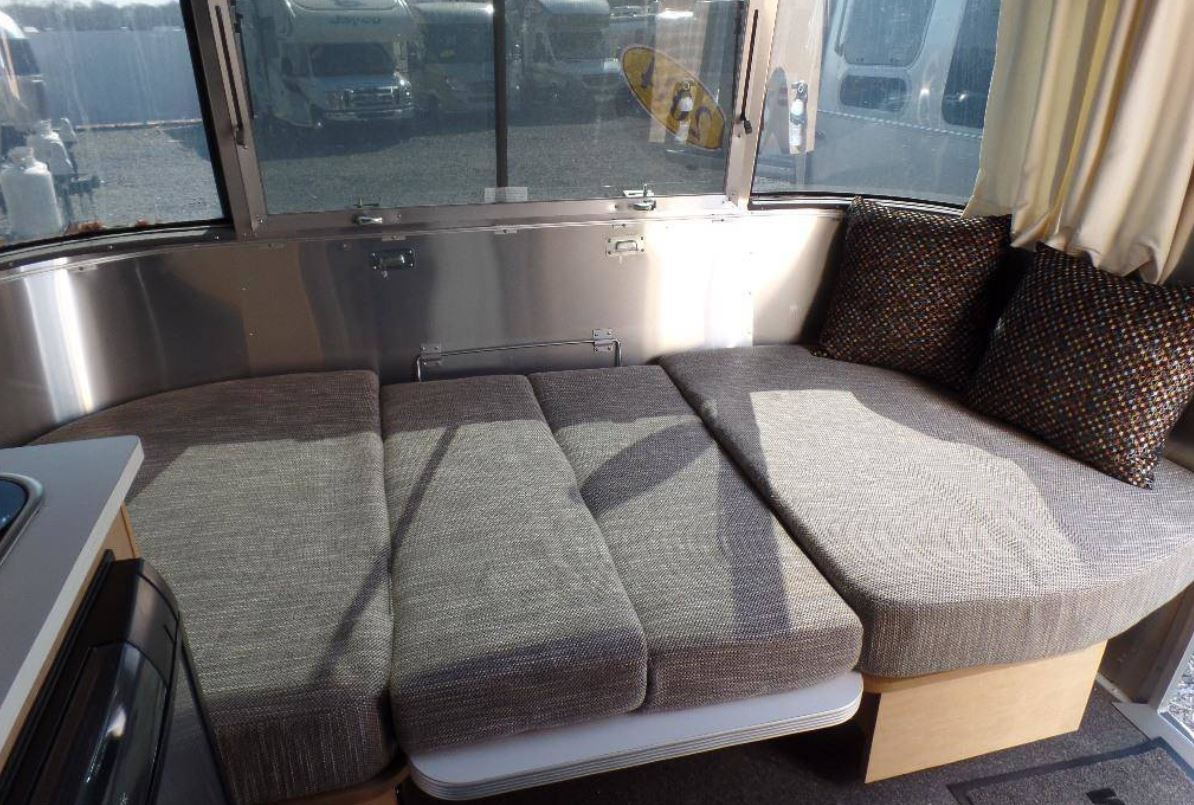 RV rental interior: Curved dinette lounge with grey fabric cushions, metallic walls, & window view of other RVs.. Airstream Sport 2015