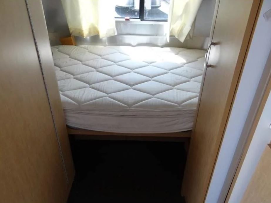 This RV rental interior shows a comfortable bed with a quilted mattress, flanked by light wood cabinets and a window.. Airstream Sport 2015