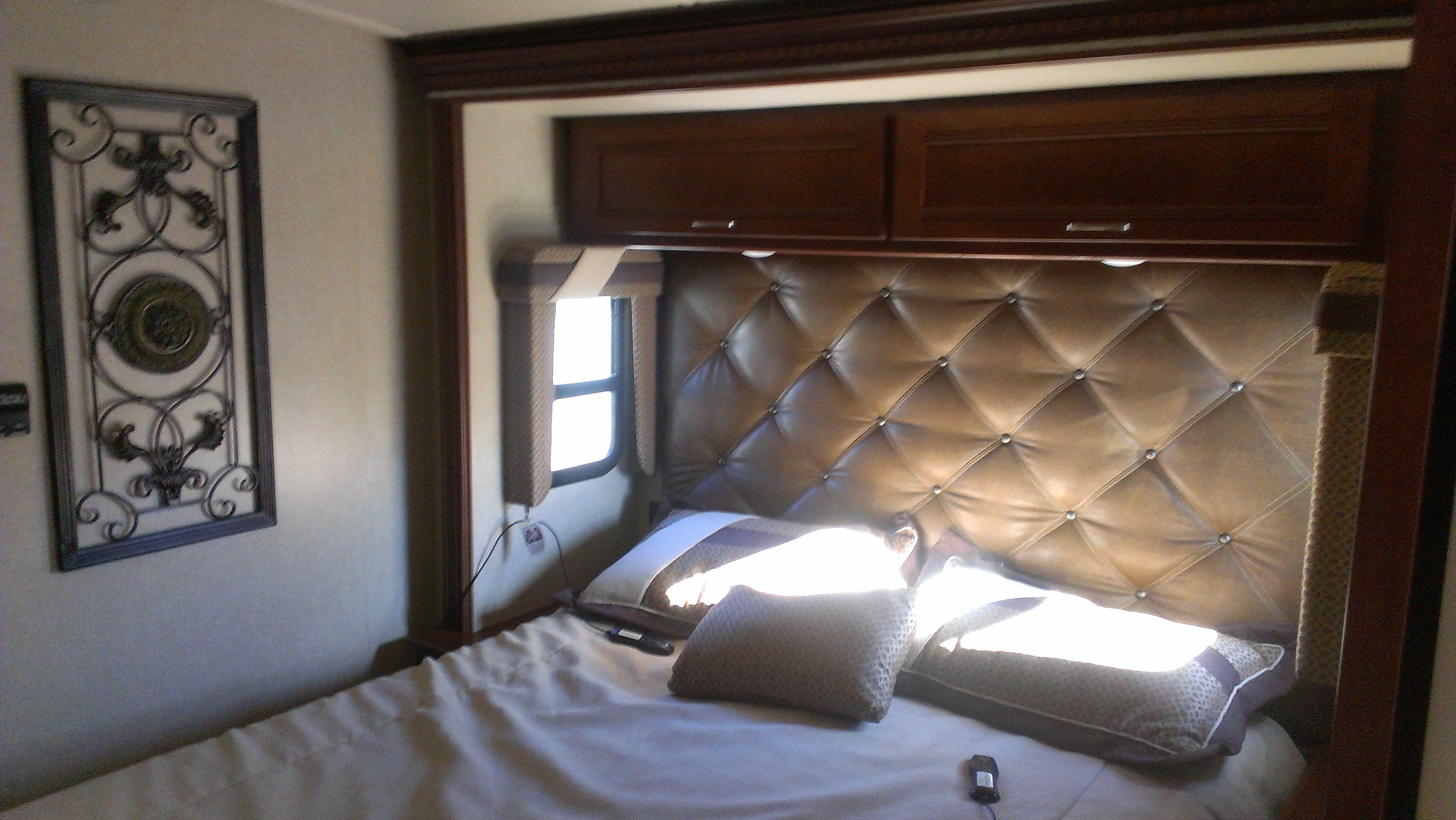 Cozy RV rental bedroom with a brown tufted headboard, overhead storage, and decorative wall art.. Itasca Solei 2014