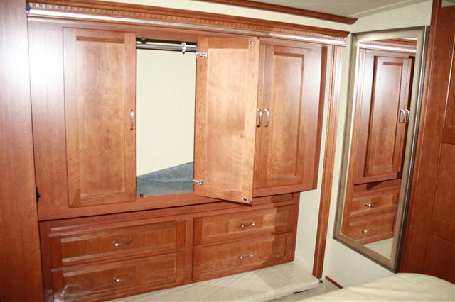 Spacious RV rental bedroom storage featuring wood cabinetry, an open wardrobe, drawers, and a full-length mirror.. Itasca Solei 2014