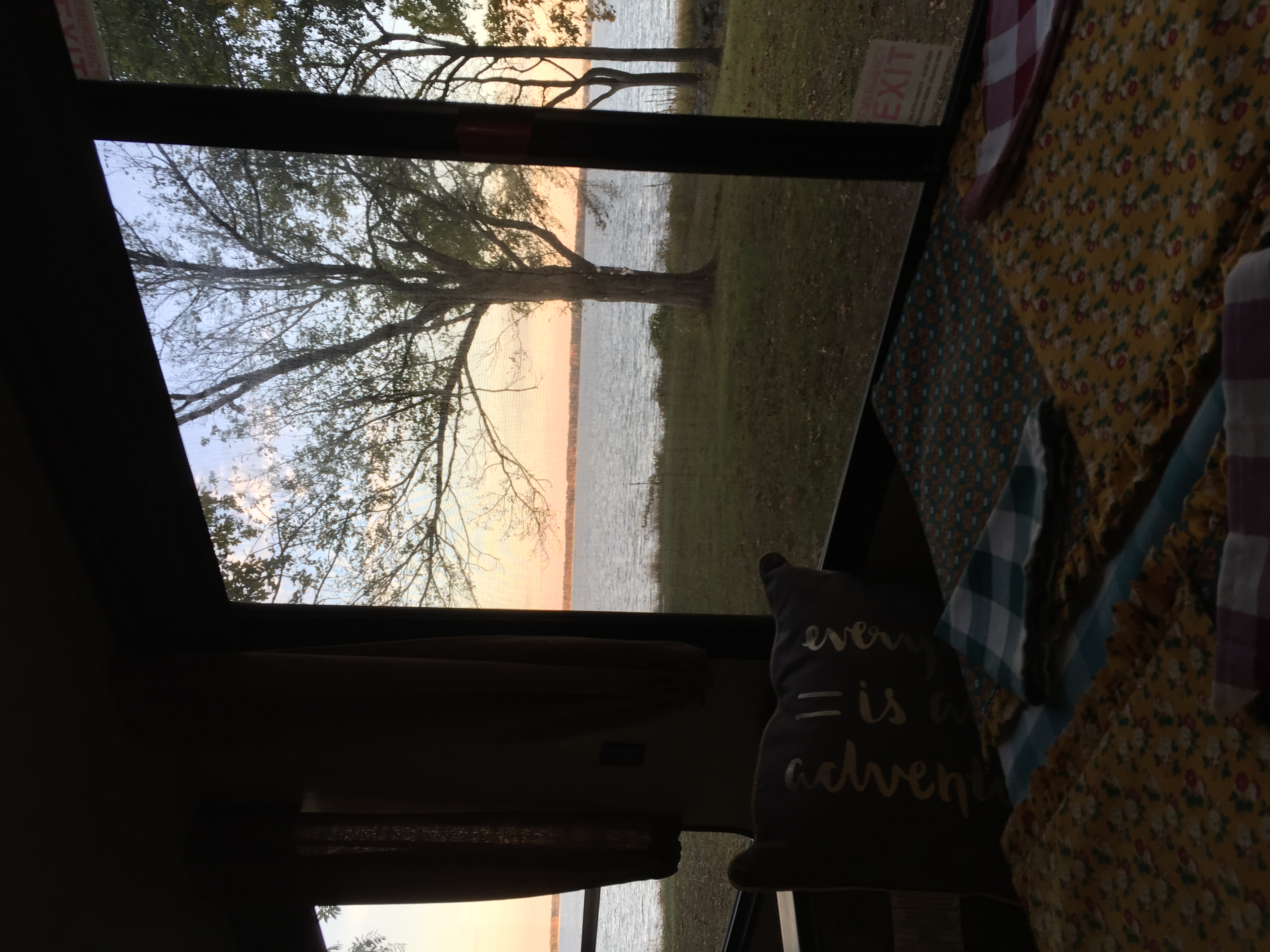 Cozy RV rental showcasing a serene lakeside sunset with silhouetted trees outside. Inside, patterned bedding and an "adventure" pillow invite comfort.. Forest River Cherokee 2018