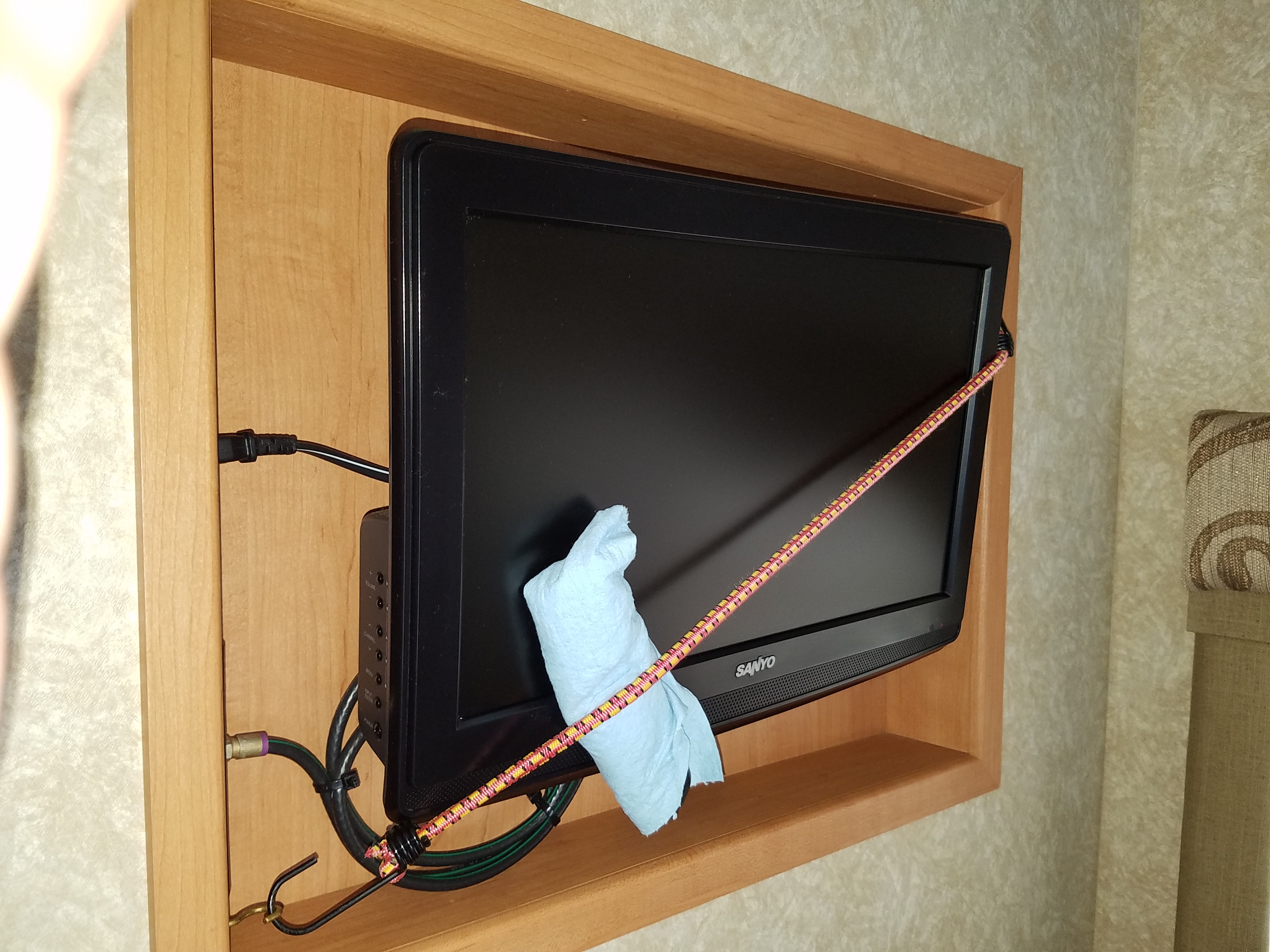 RV rental TV setup: a Sanyo screen in a wood cabinet, secured with a bungee cord, with a cleaning cloth.. Four Winds Chateau Sport 2008