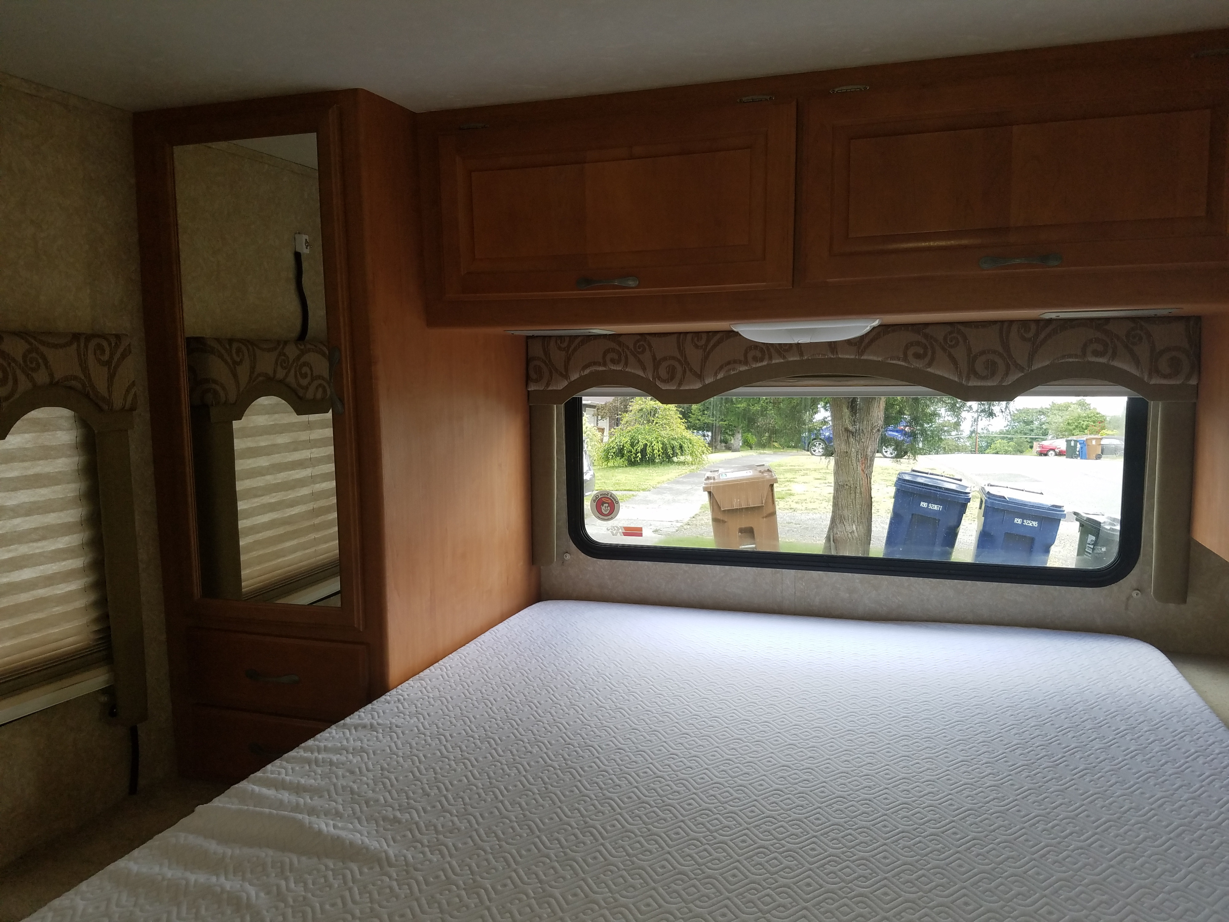Inside an RV rental bedroom: a comfy white mattress, warm wood cabinetry, and a window view of the outdoors.. Four Winds Chateau Sport 2008