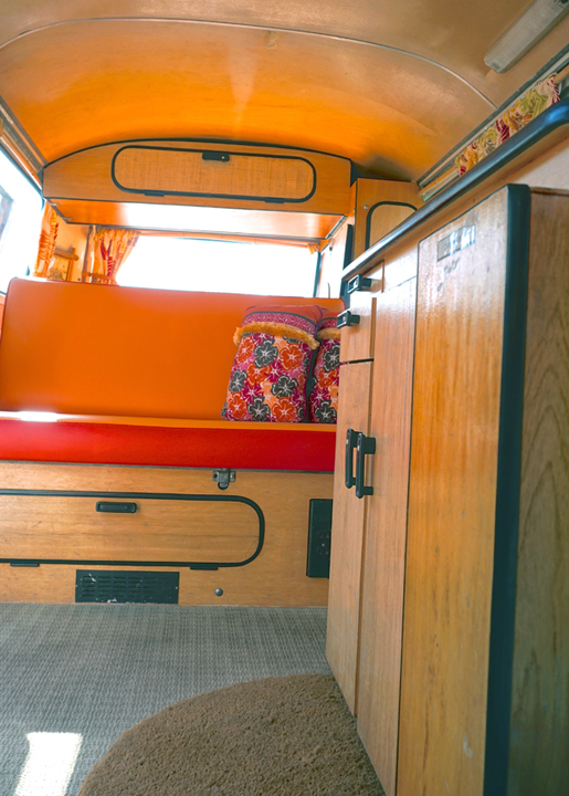 Cozy RV rental interior: vibrant orange bench seat, floral pillows, & wood cabinets. Ready for adventure!. Volkswagen Westfalia 1978