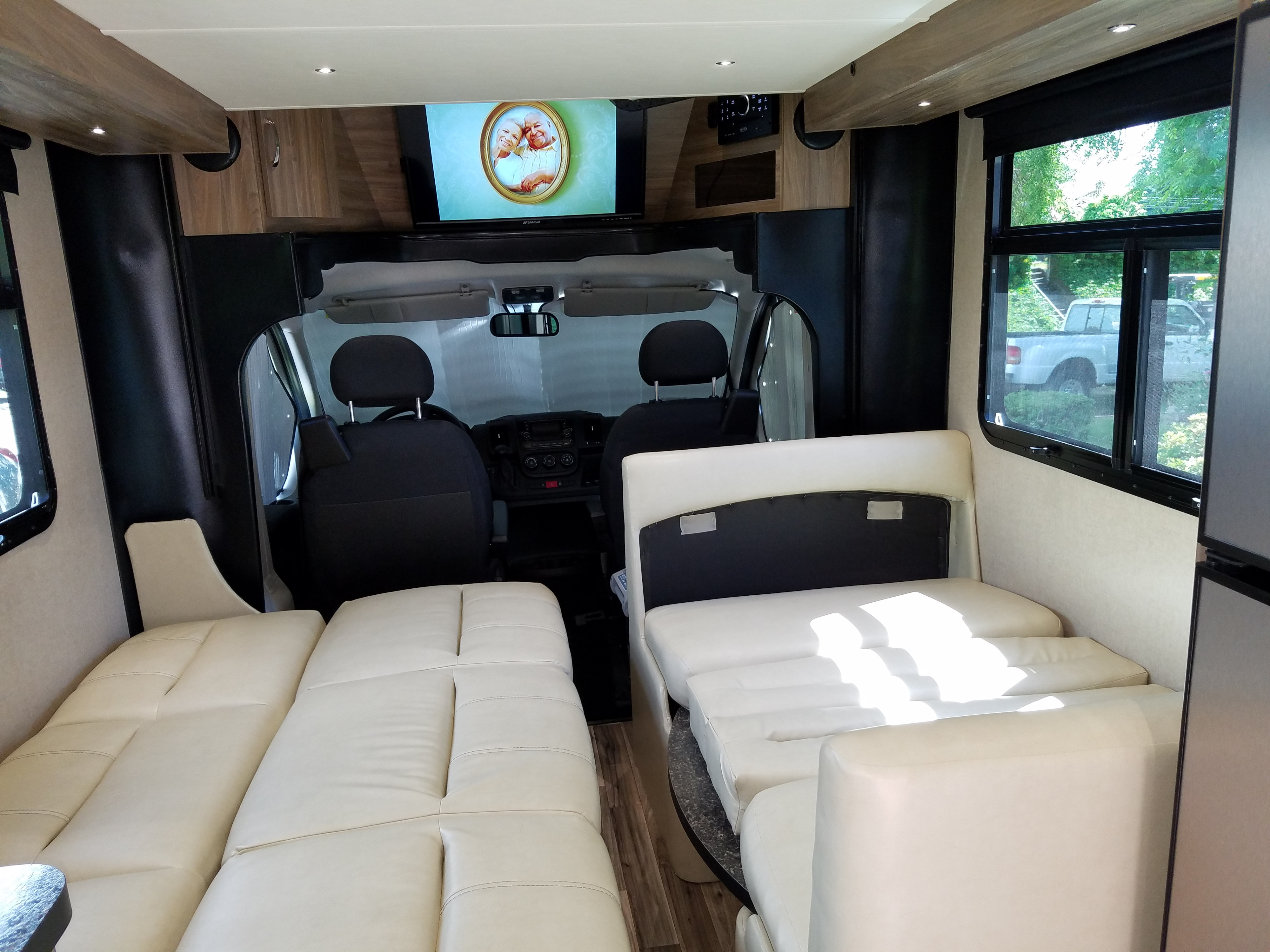 Spacious RV rental interior with cream sofas converting to beds, facing cockpit & TV.. Dynamax REV 24RB 2018
