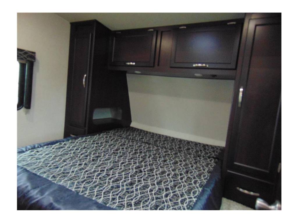 Cozy RV rental bedroom featuring dark wood storage cabinets and a stylish patterned comforter on the bed.. Genesis Supreme Rv Genesis Supreme 2019