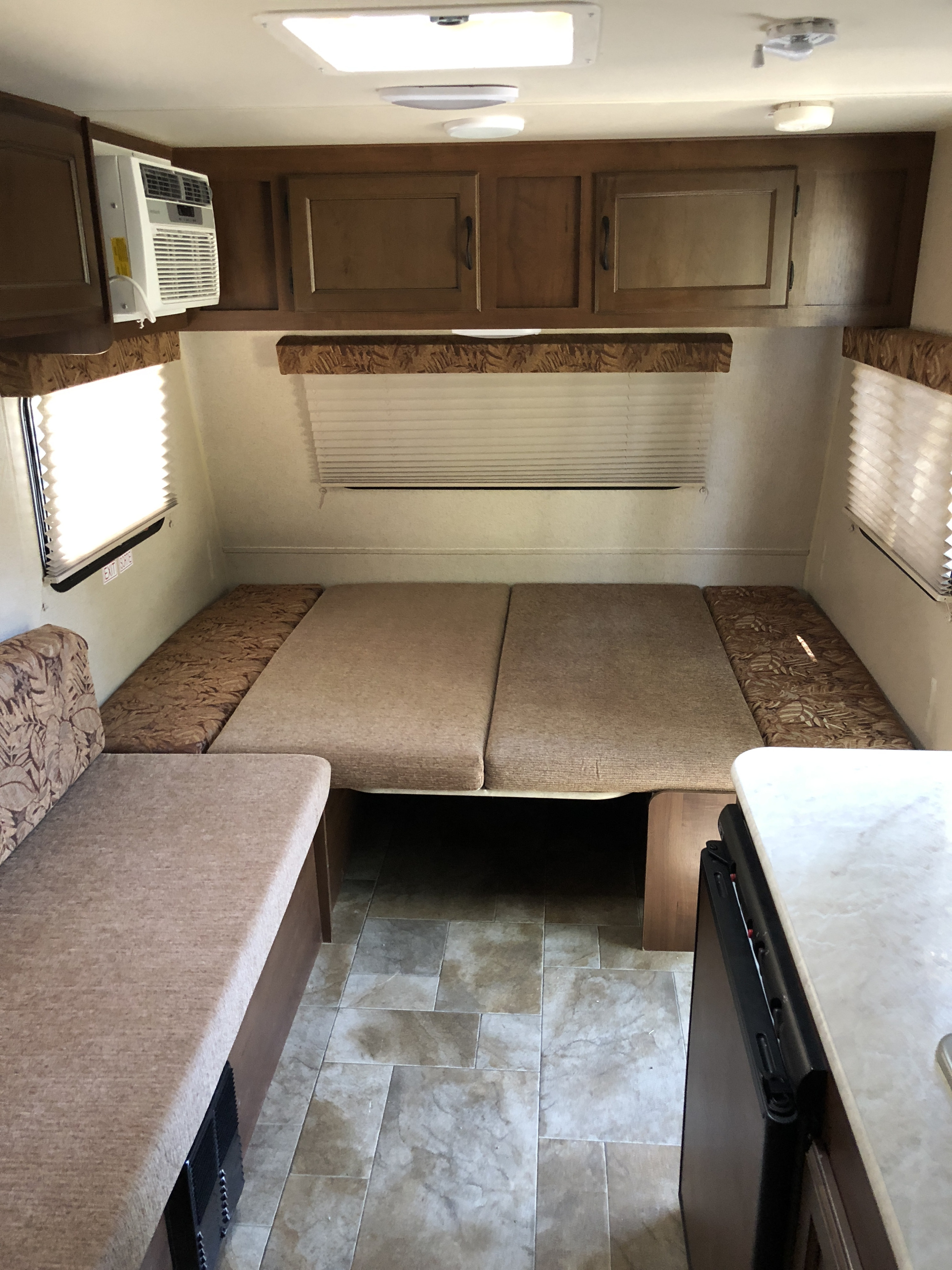 RV rental interior: dinette converts to bed, with overhead cabinets, windows with blinds, AC unit, and tiled floor.. Jayco Jay Flight SLX 2015