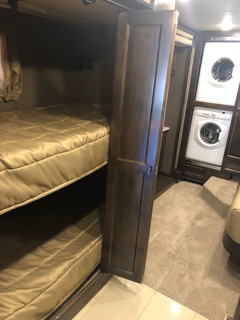 RV rental interior with bunk beds on left, dark wood partition, and a stacked washer/dryer unit on right.. Tiffin Motorhomes Allegro Red 2018