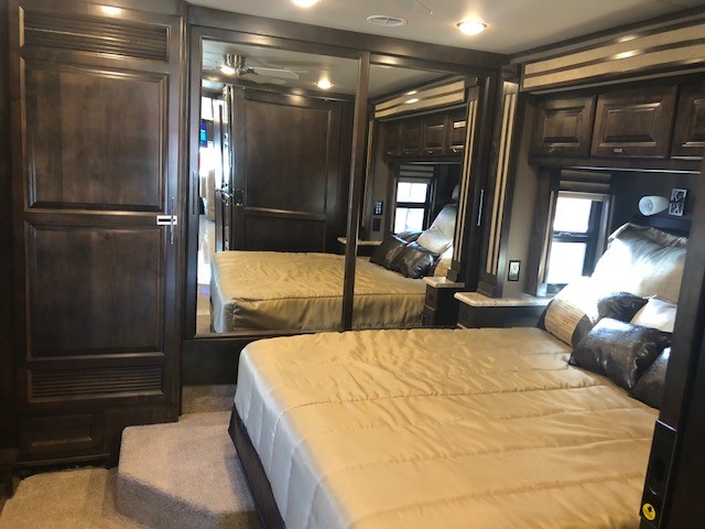 Spacious RV rental bedroom featuring a large bed, dark wood cabinetry, and reflective mirrored closet doors. Steps lead to the bed.. Tiffin Motorhomes Allegro Red 2018