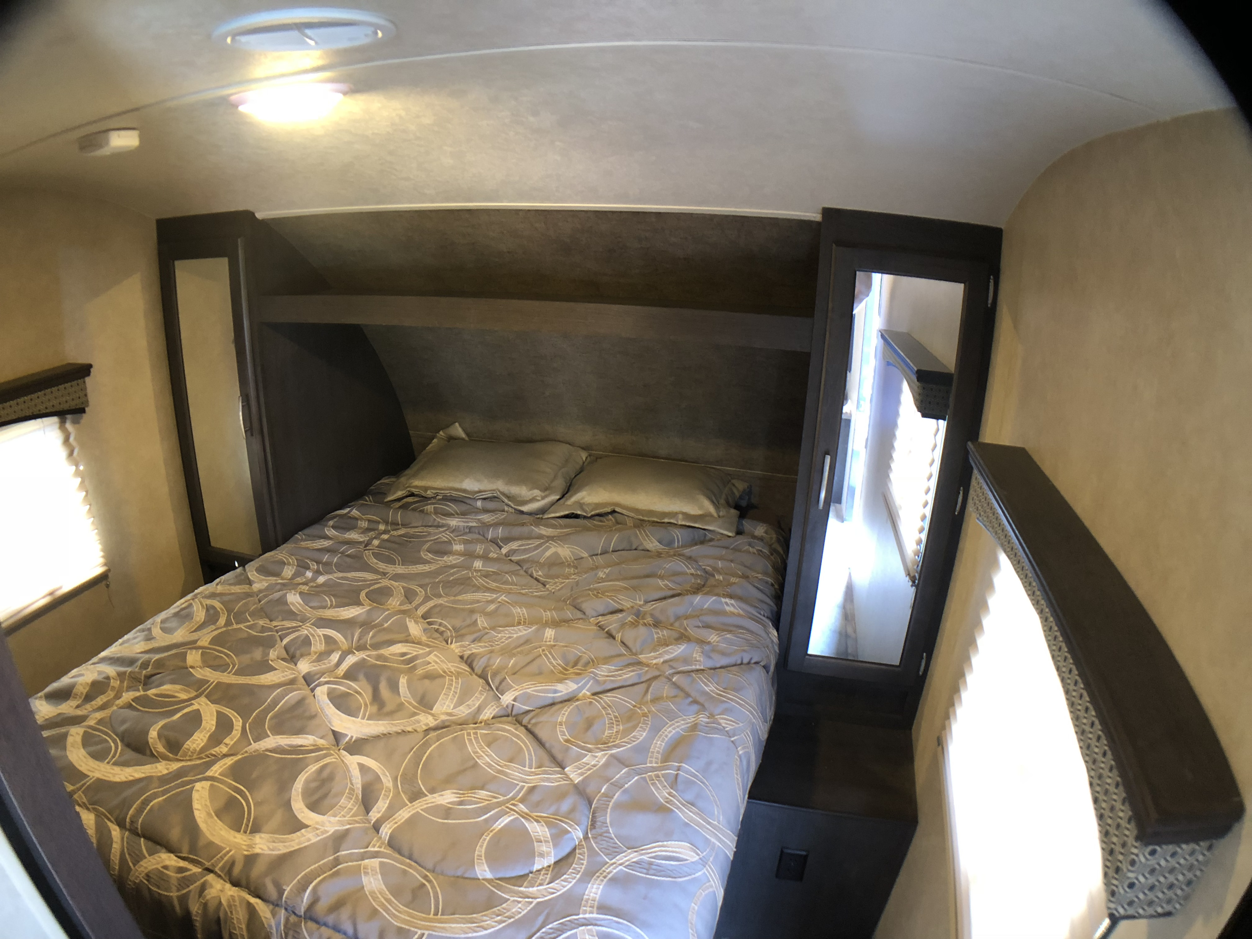 Cozy RV rental bedroom showcasing a comfy bed with patterned comforter, overhead storage, and mirrored cabinets.. Forest River Evo 2017