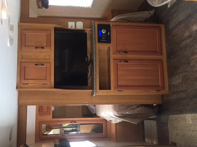 Cozy RV rental interior featuring a wooden entertainment center with TV, stereo, and adjacent bedroom.. KZ Spree Connect 2015