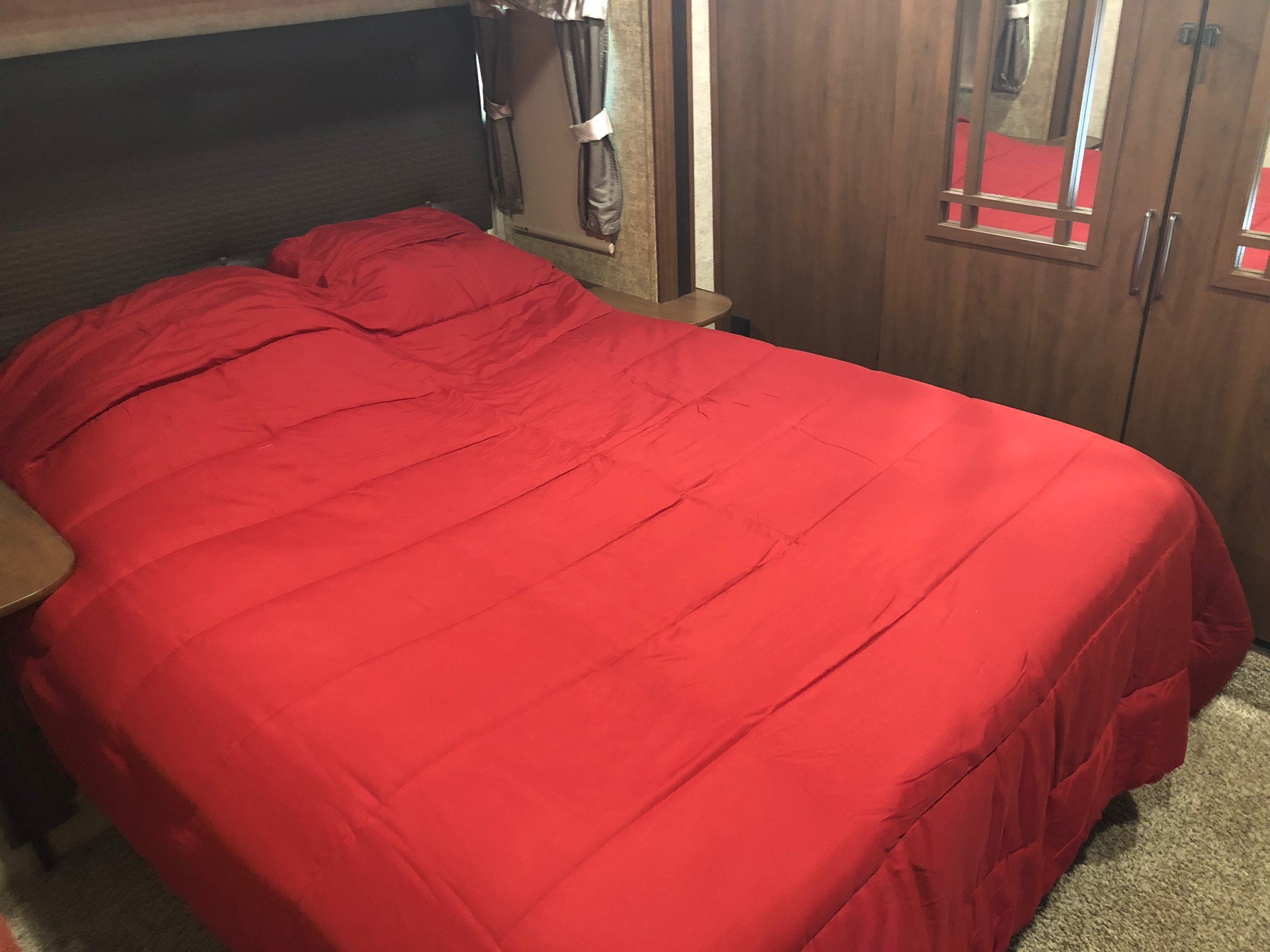 Cozy RV rental bedroom featuring a vibrant red bed, pillows, and a built-in mirrored wardrobe.. Forest River Sierra 2017