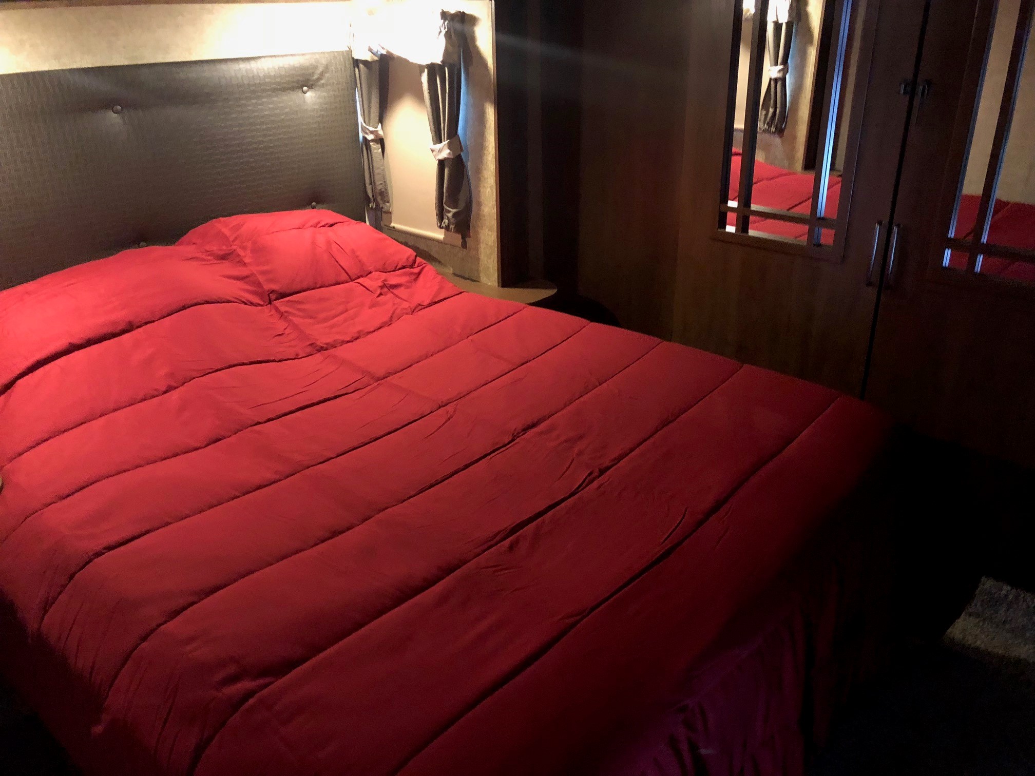 Cozy RV rental bedroom featuring a red comforter, padded headboard, and mirrored closet.. Forest River Sierra 2017