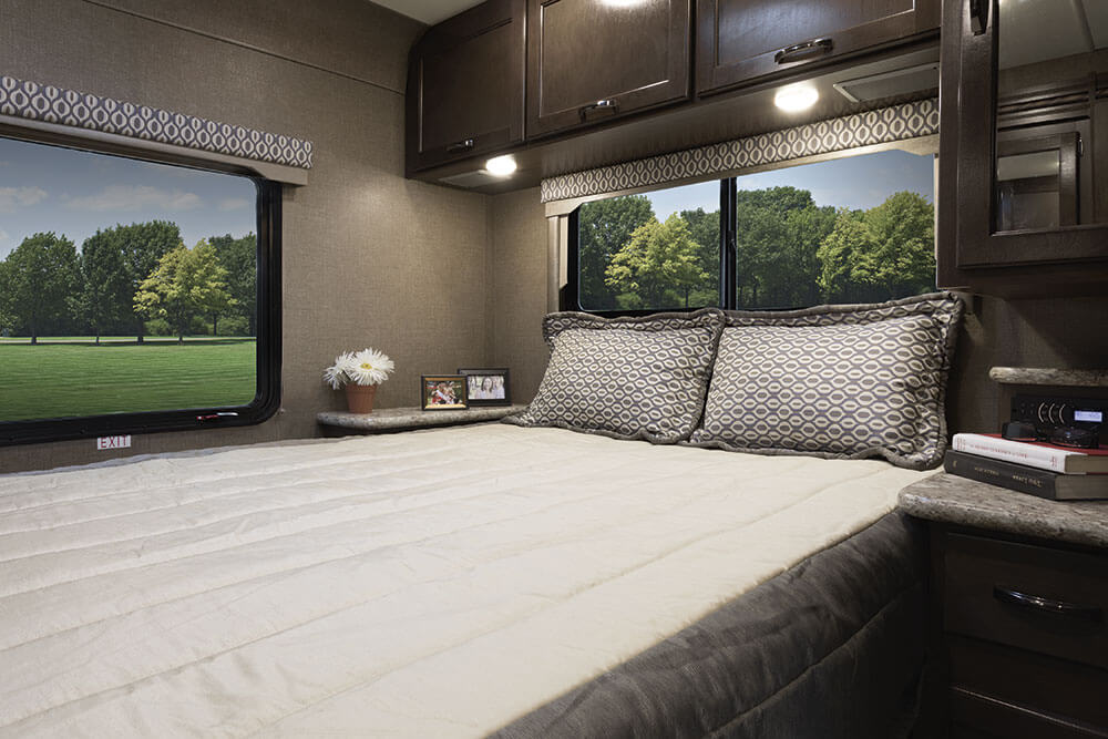 Comfortable RV rental bedroom featuring a large bed, overhead cabinets, and panoramic window views of nature.. Thor Freedom Elite 2018