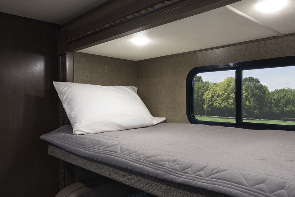 RV rental: Cozy bunk bed with pillow, quilt, and window view of green trees. Ideal for camping.. Thor Freedom Elite 2018