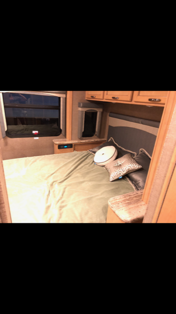 Cozy RV rental bedroom features a comfortable bed, window, and wooden overhead cabinets for storage.. Thor Motor Coach A.C.E 2017