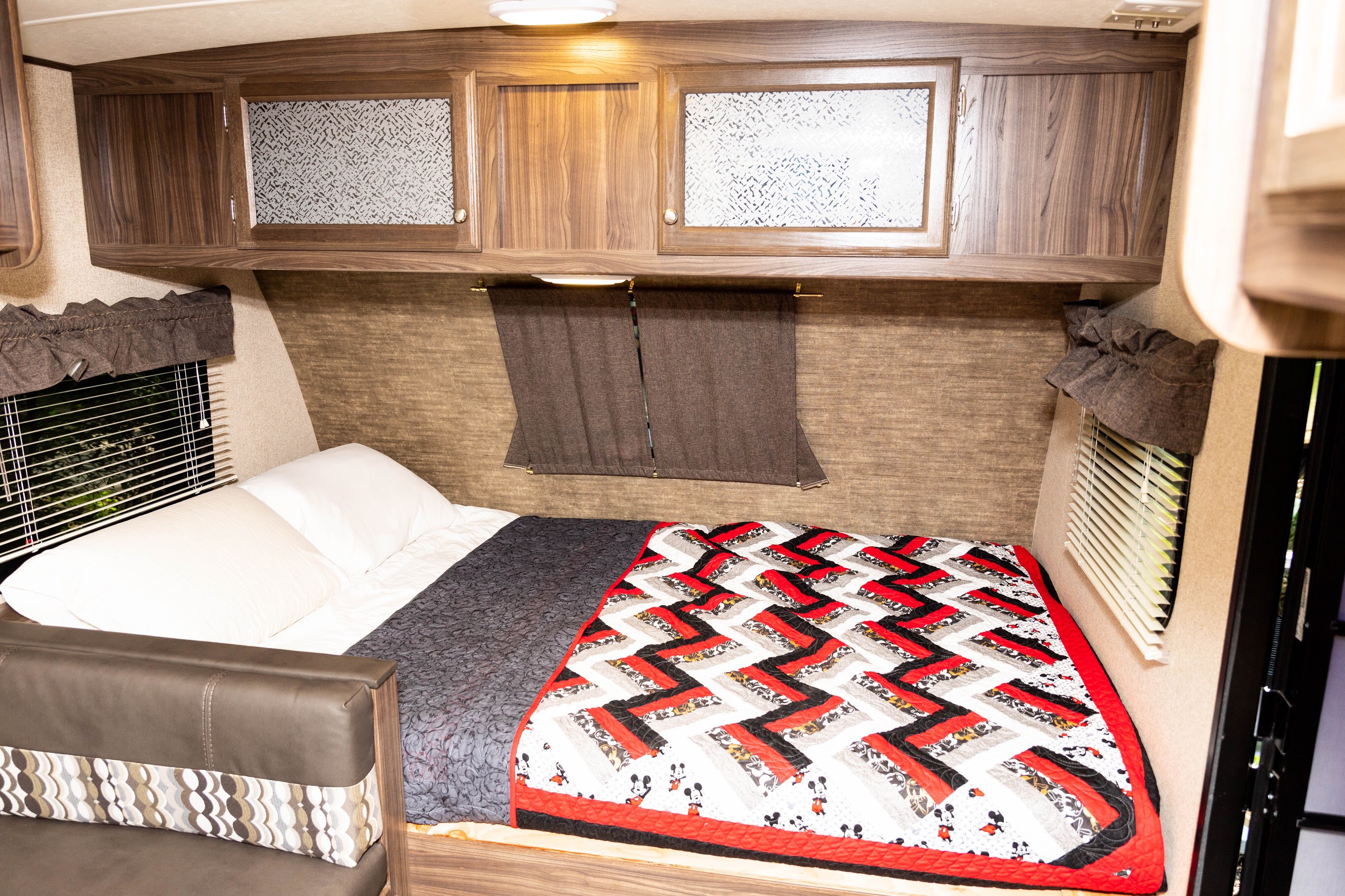 Inside a comfy RV rental: bed with colorful Mickey Mouse quilt, wood cabinets & window.. Apex Nano 185BH 2019