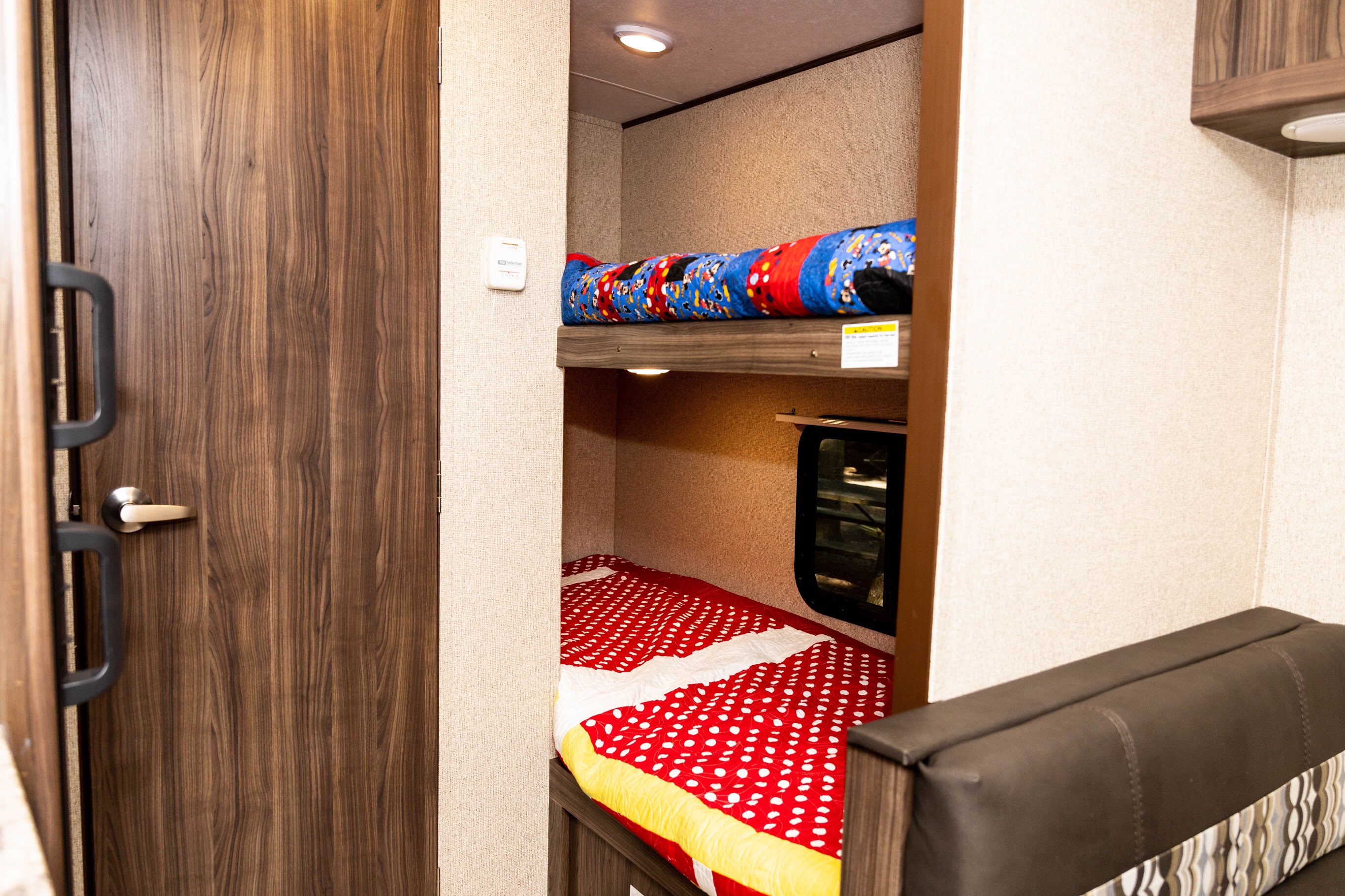 Inside an RV rental, showing a bunk bed sleeping area with themed blankets (Mickey Mouse, polka dot), and a side door.. Apex Nano 185BH 2019