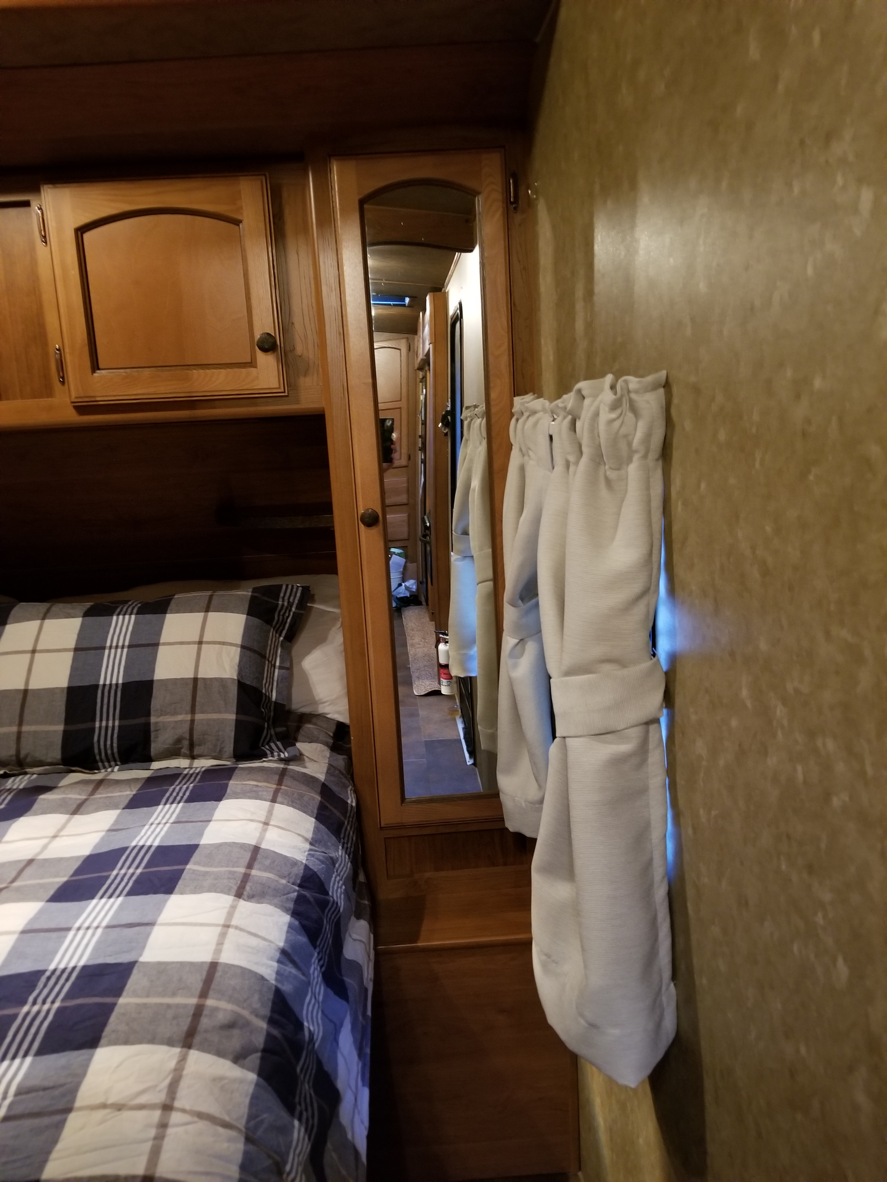 RV rental bedroom with plaid bedding, wood cabinets, full-length mirror reflecting the aisle, and white tie-back curtains.. Crossroads Sunset Trail 2015
