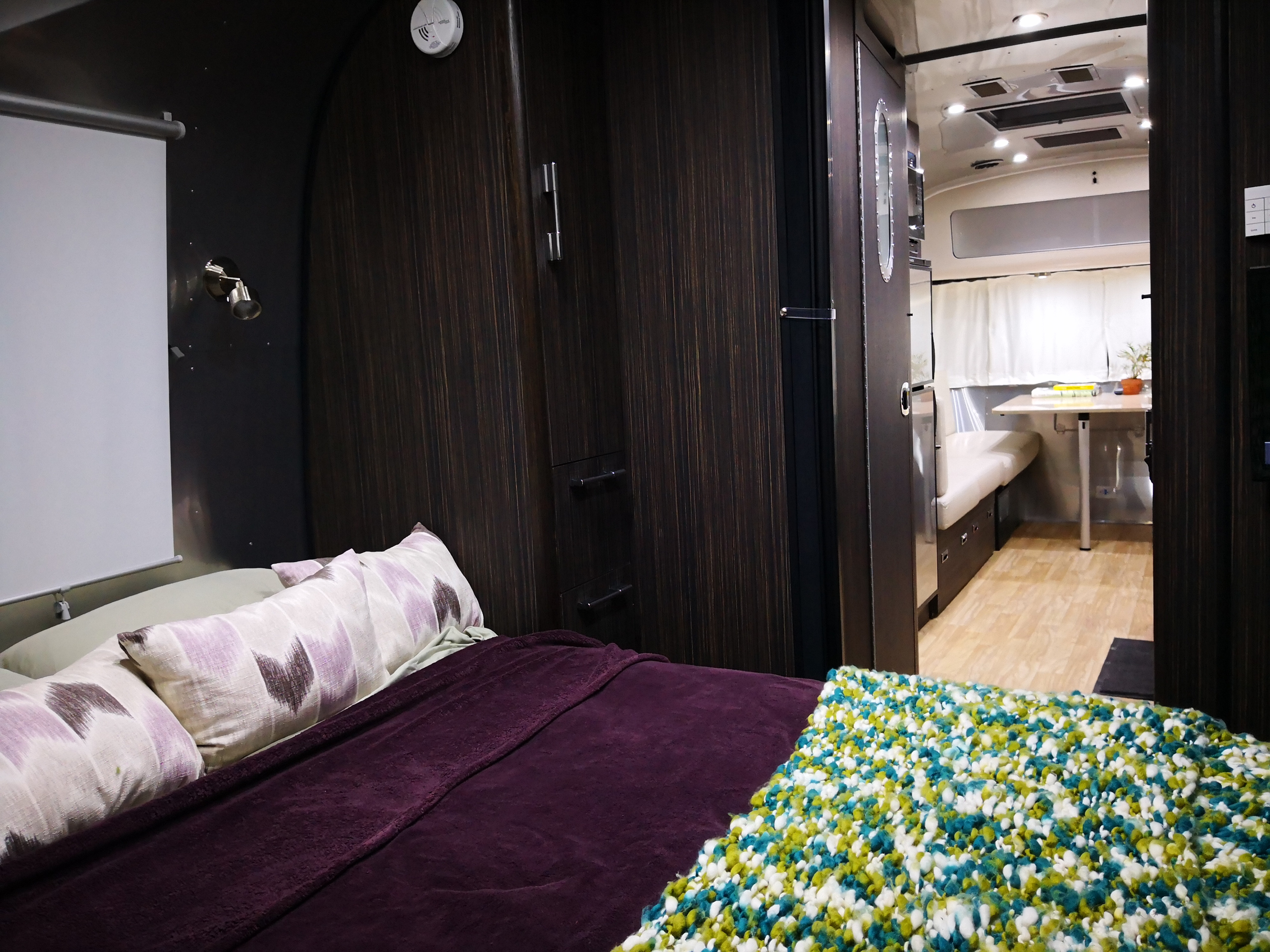 Cozy RV rental interior featuring a bedroom with colorful blankets and a view into the dinette area.. Airstream International 2018