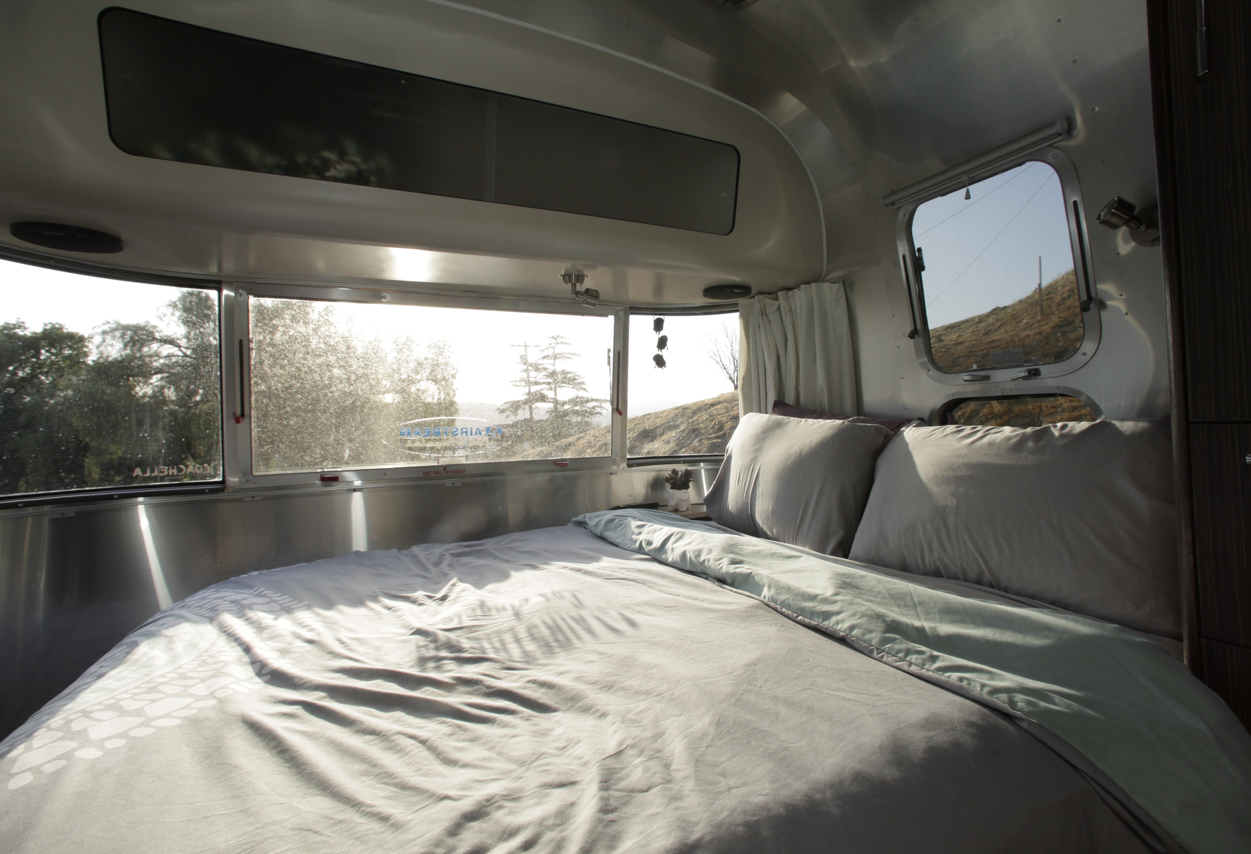 Bright Airstream rv rental bedroom: comfy bed, shiny aluminum walls, and scenic outdoor views from large windows.. Airstream International 2018