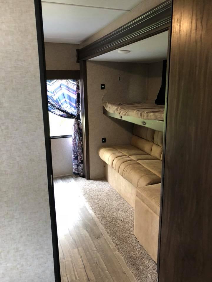 Inside an RV rental bunkhouse: A cozy space with a lower sofa and upper bunk, dual flooring, and a patterned window curtain.. Forest River Cherokee 2018