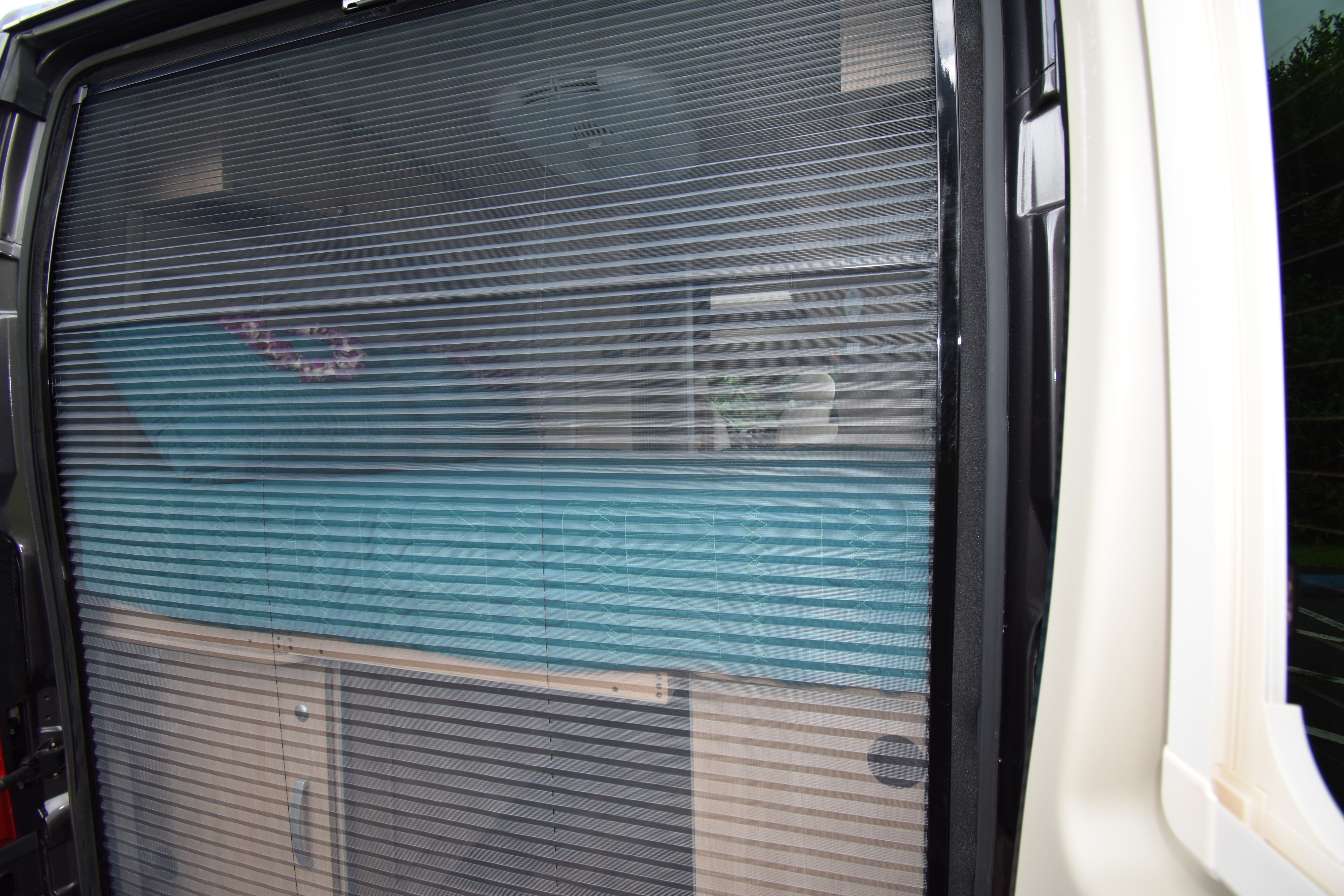 RV rental: Pleated screen and blind on a camper van side door, offering privacy to the interior with blue bedding.. Hymer Aktiv 2018