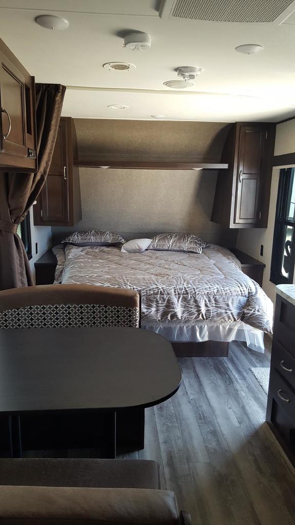 RV rental interior showing a comfortable bedroom with patterned bedding and overhead cabinets, adjacent to a cozy dining area.. Jayco Jay Flight 2018