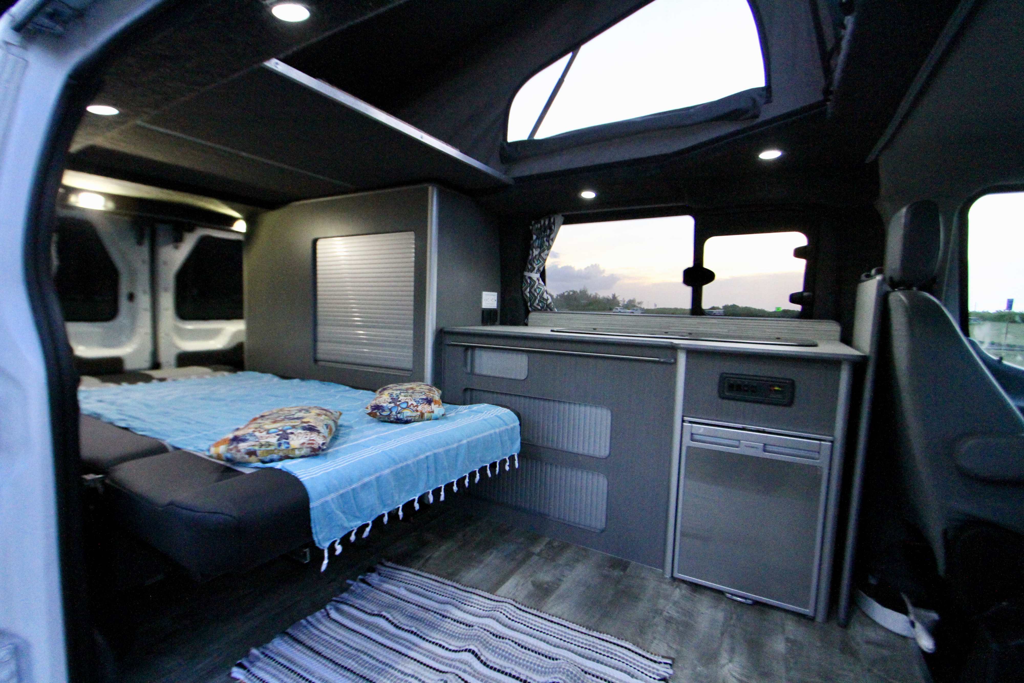 Spacious camper van interior for rv rental, showing a comfy bed, compact kitchen, and pop-top for bright adventures.. Ford Transit 2017