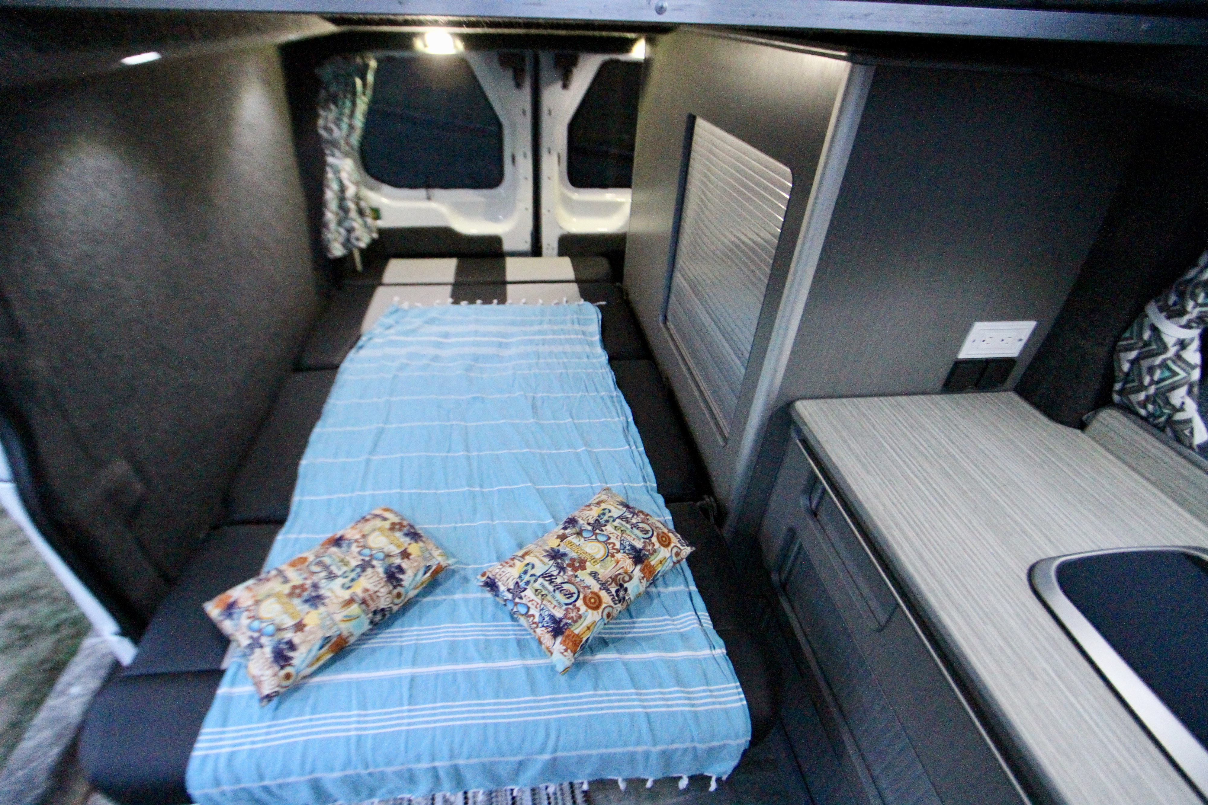 Spacious RV rental interior featuring a comfy bed with blue blanket, colorful pillows, and a compact kitchen counter.. Ford Transit 2017