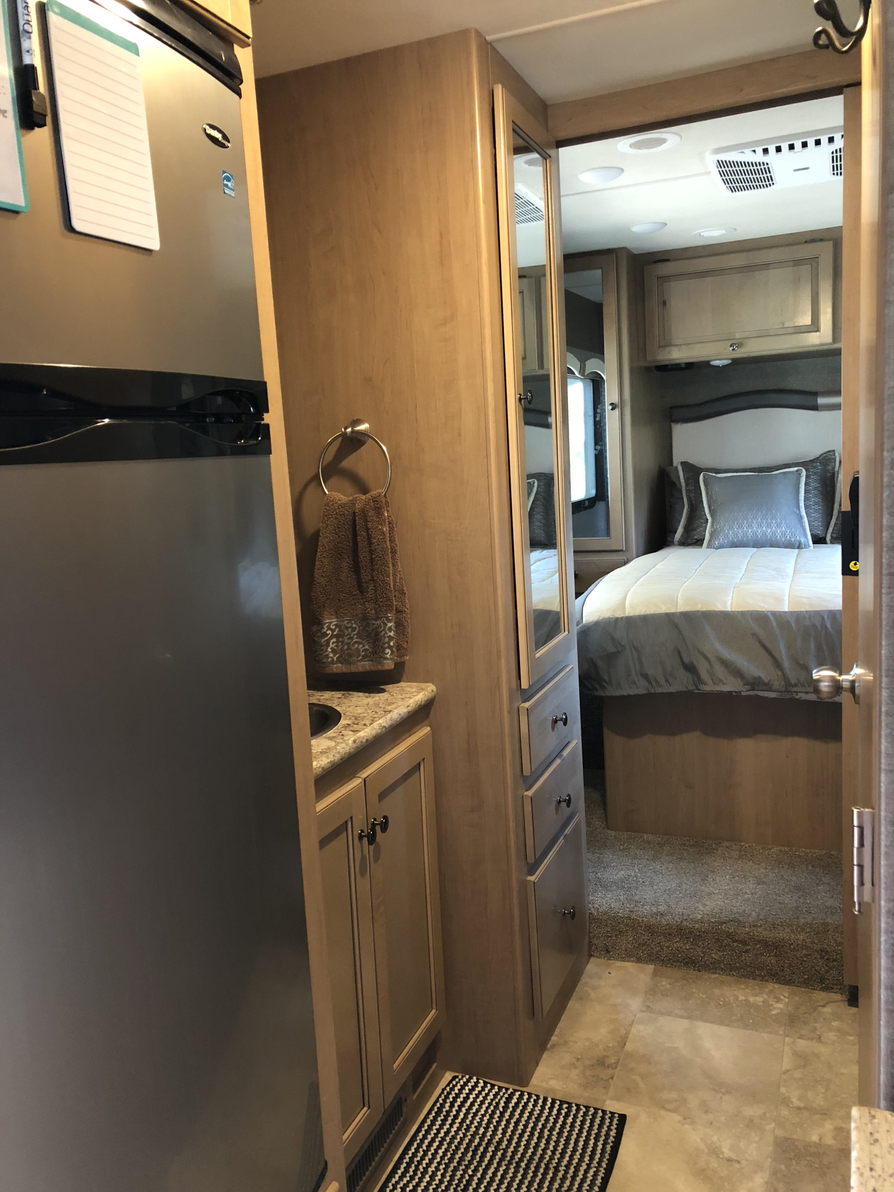 Cozy RV rental interior featuring a bedroom, compact fridge, and small vanity sink.. Thor Windsport 2018