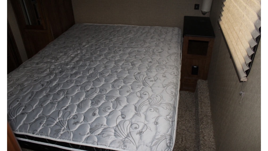 Comfortable RV rental bedroom featuring a large quilted mattress, nightstand, and window blinds, ready for your trip.. Coachman Chaparral 2017