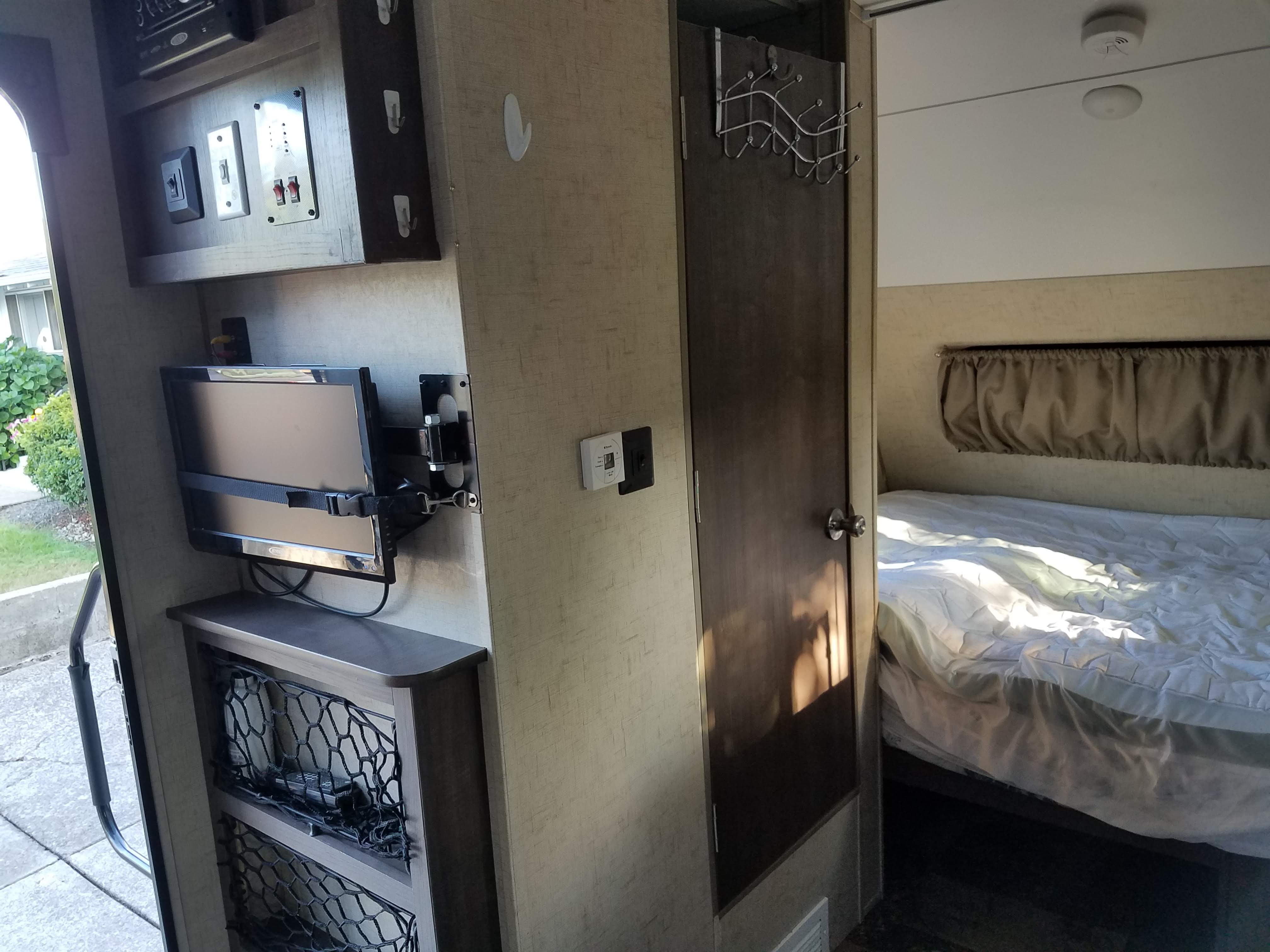An RV rental interior: A mounted TV, control panel, and a cozy bedroom are visible, with an open entry door outside.. Forest River R-Pod 2016