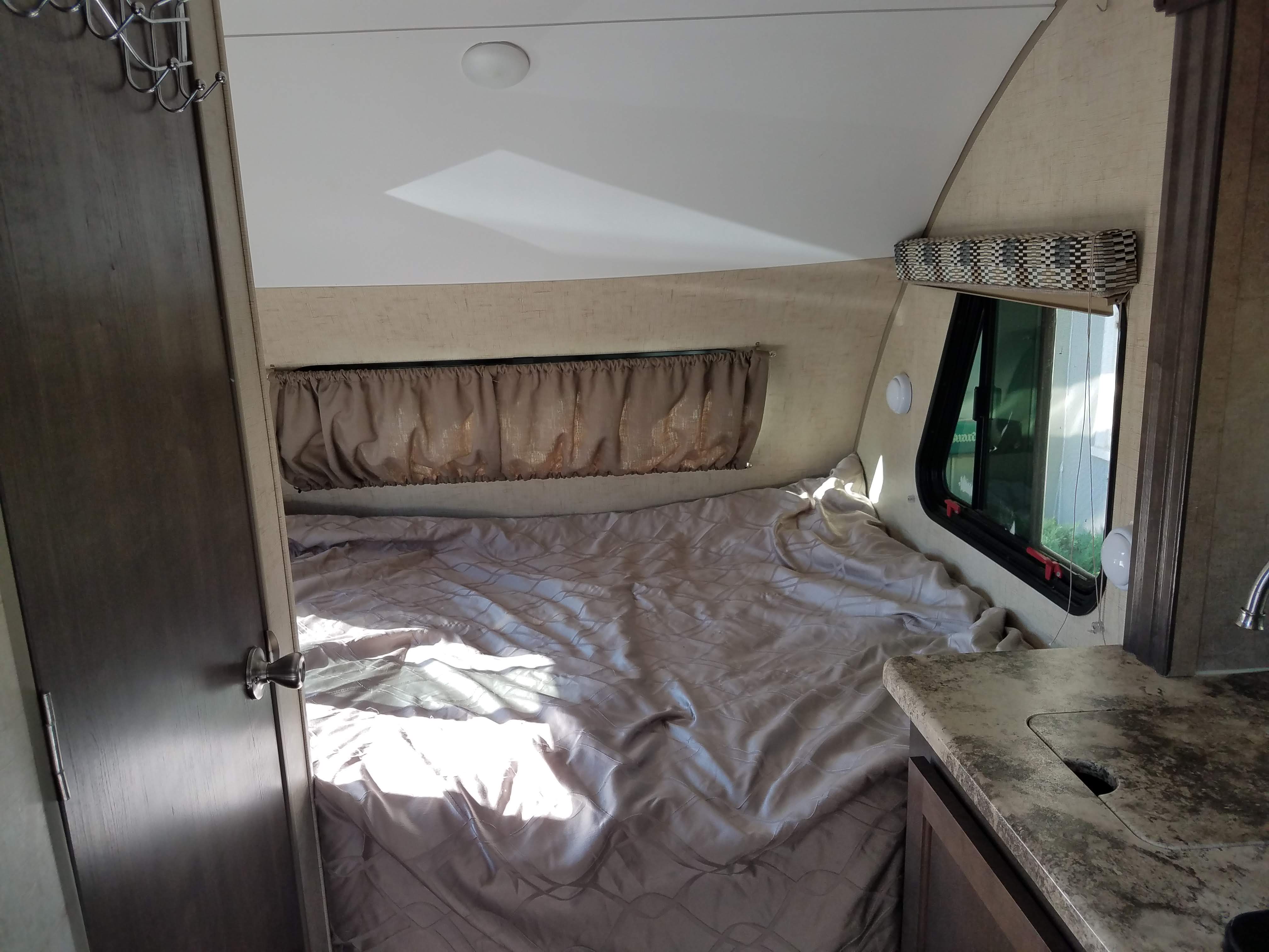 Cozy RV rental interior, featuring a bed bathed in sunlight, a small window, and a compact counter with a sink.. Forest River R-Pod 2016