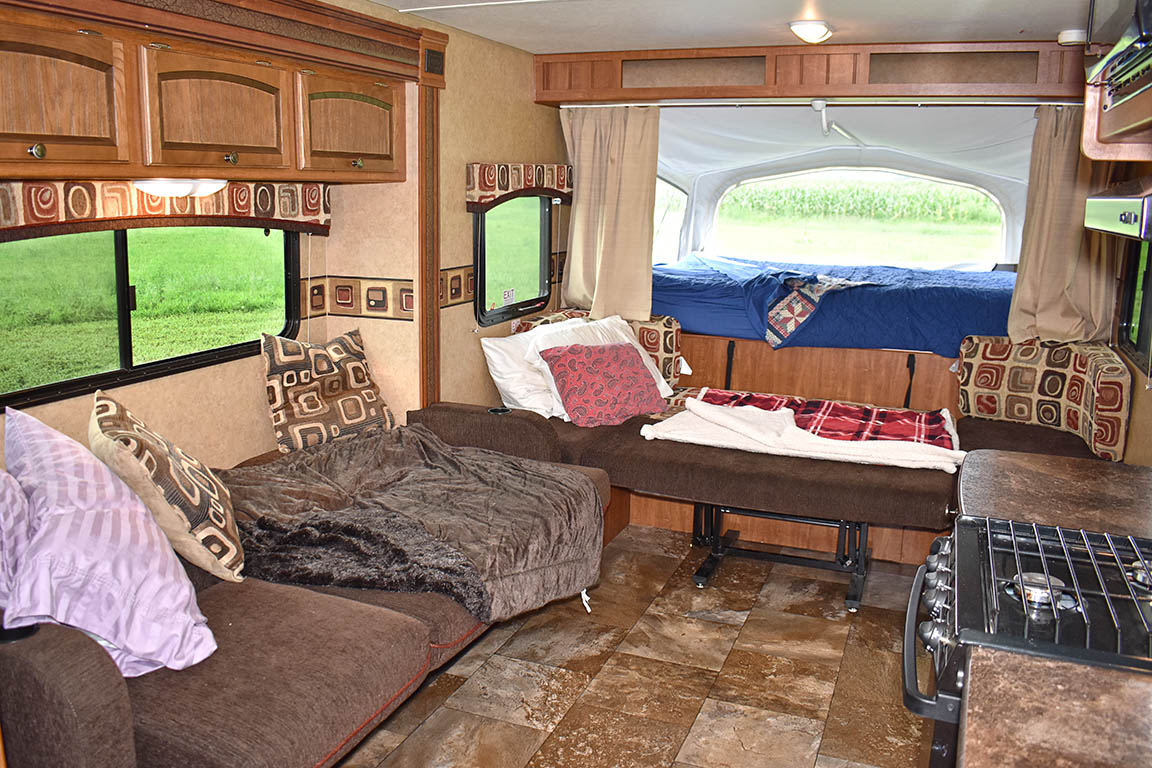 Explore this spacious RV rental interior! Features a cozy living area with sofa, kitchen, and a comfortable pop-out bed overlooking nature.. Jayco Jay Feather Ultra Lite 2013