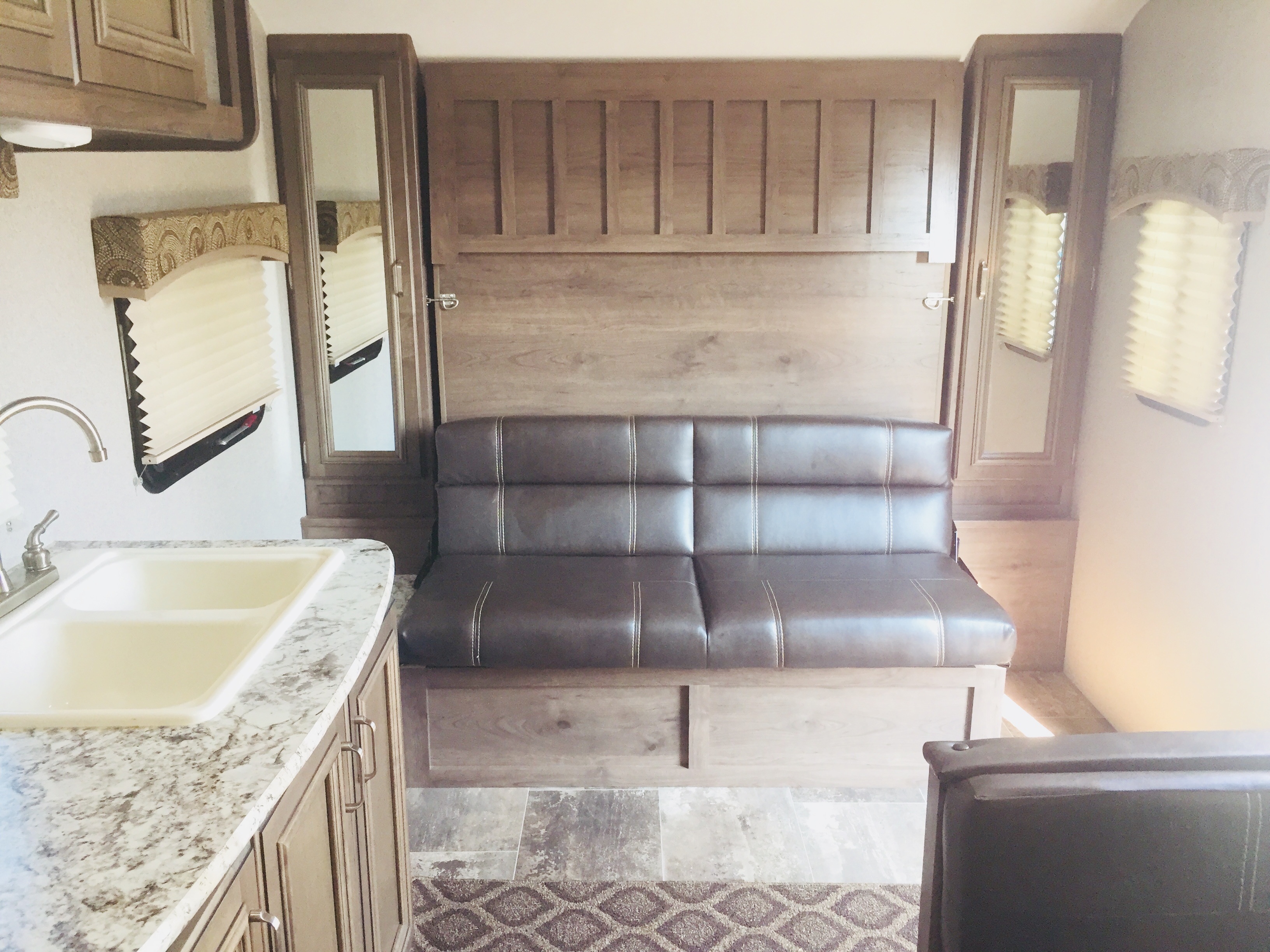 Experience a compact RV rental interior with a comfortable sofa, kitchen counter with sink, and upright murphy bed.. Keystone Passport 2018
