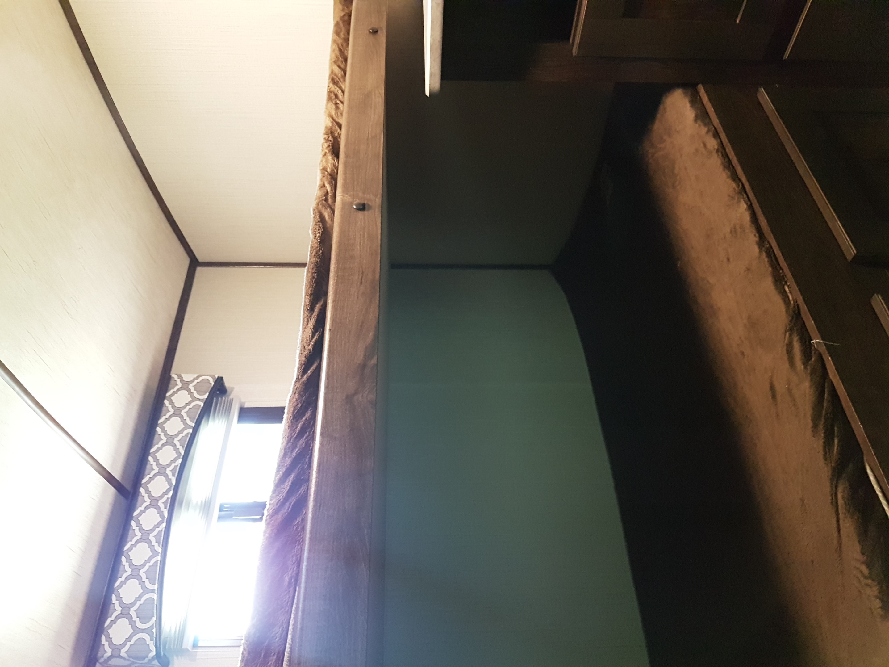 Compact RV rental interior featuring a bright window with patterned curtains, a wooden bunk frame, and light-colored walls.. Cruiser Rv Corp Radiance 2019