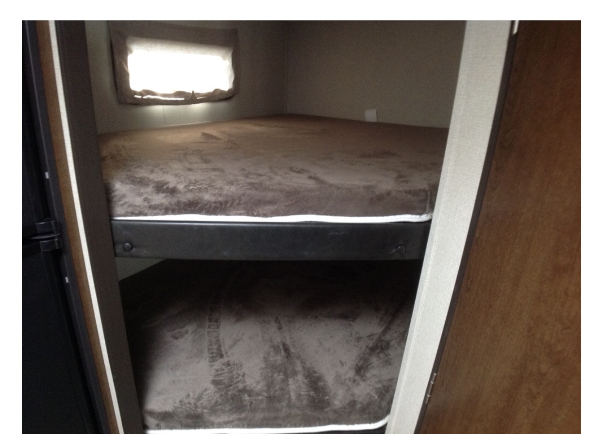 Inside an RV rental, a compact sleeping area features two bunk beds with brown bedding and a window.. Forest River Tracer 2019