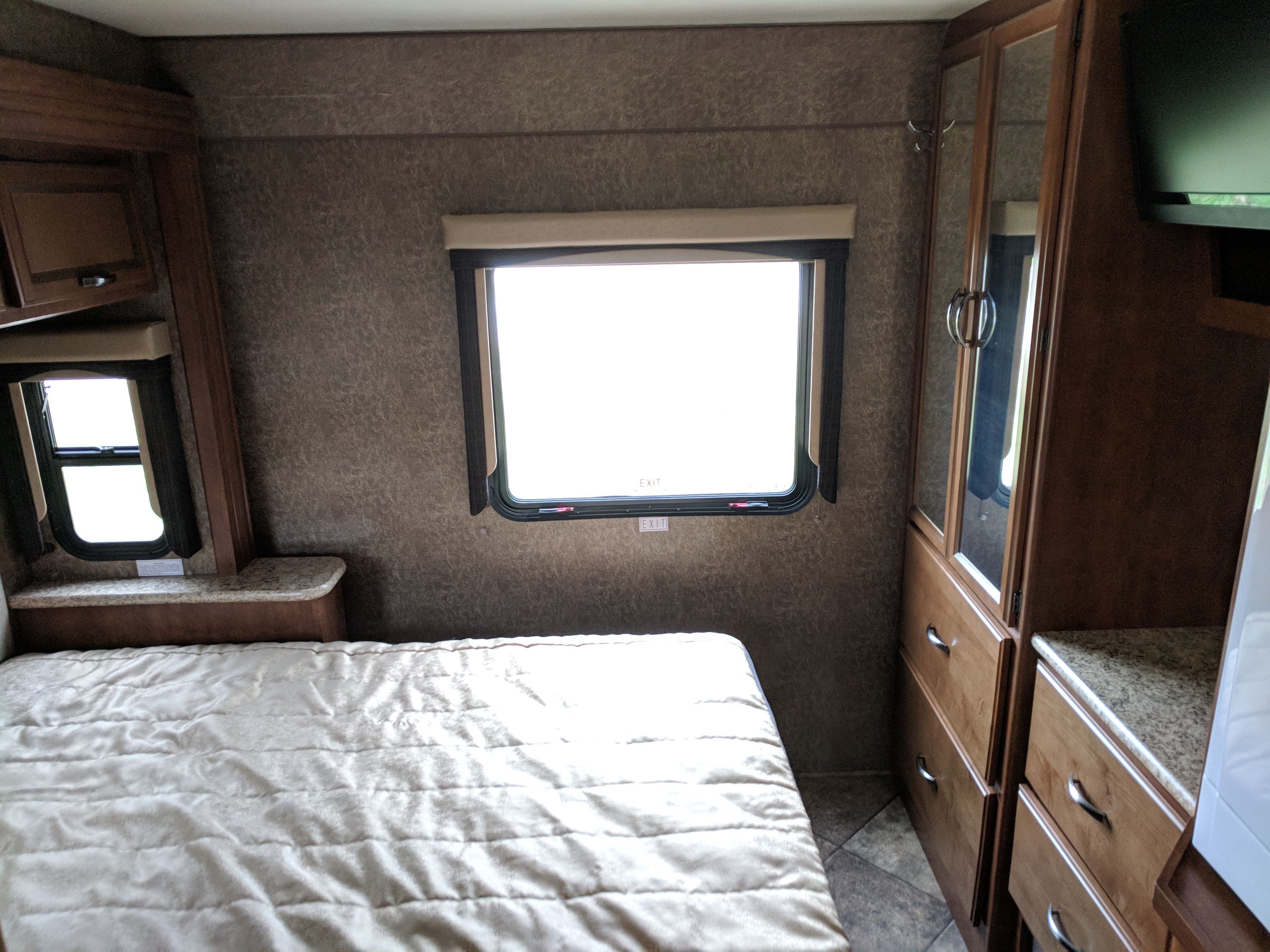 Cozy RV rental bedroom: features a comfortable bed, bright windows, and ample built-in storage with a TV.. Thor Motor Coach A.C.E 2015