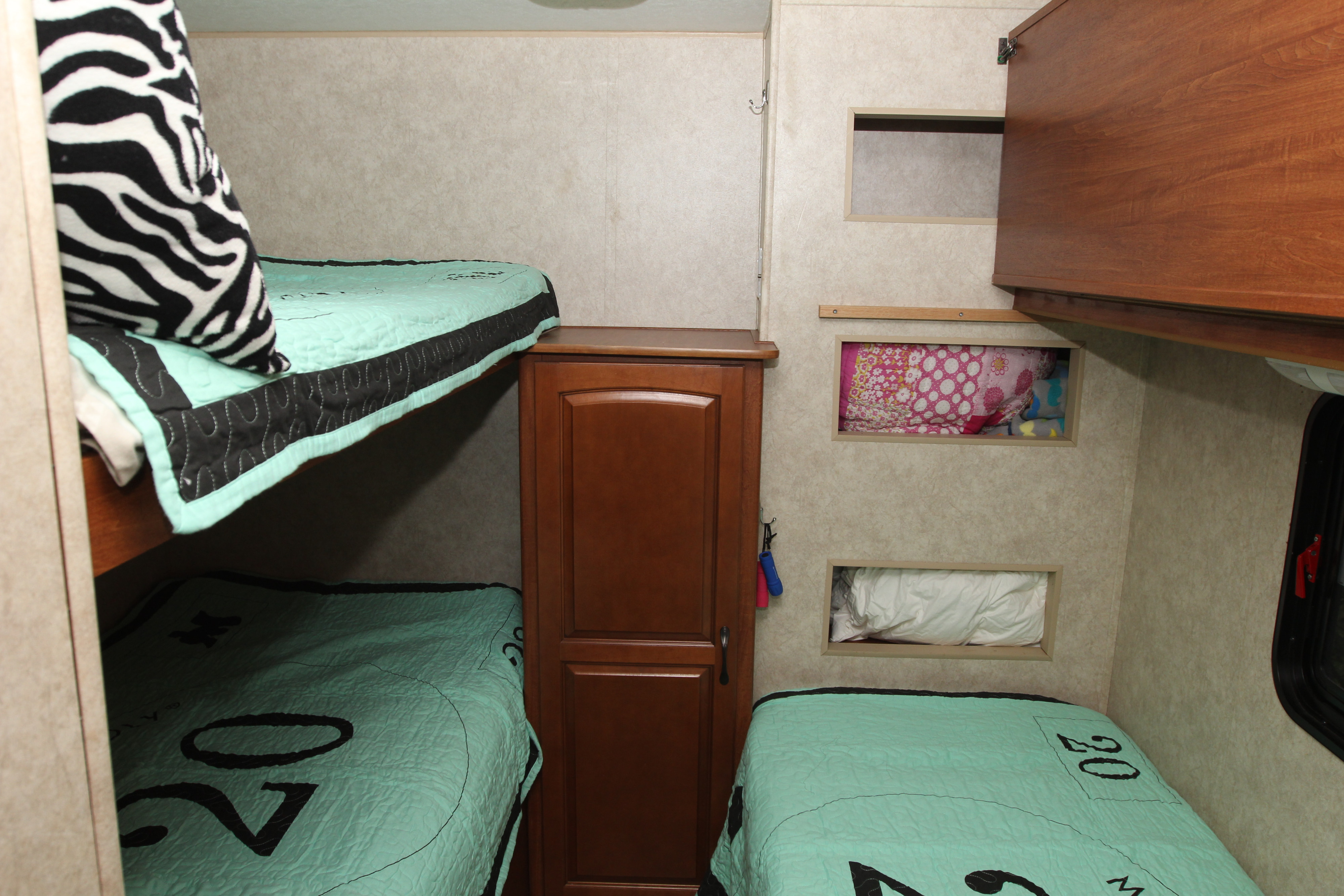 RV rental bedroom with bunk beds and another single bed, all with mint green bedding. Features include storage cubbies and a cabinet.. Forest River Surveyor 2010
