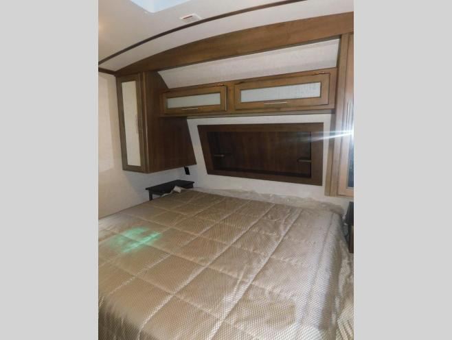 Compact RV rental bedroom with a quilted bed and built-in wooden storage cabinets, ideal for road trips.. Keystone Cougar Half-Ton 2019