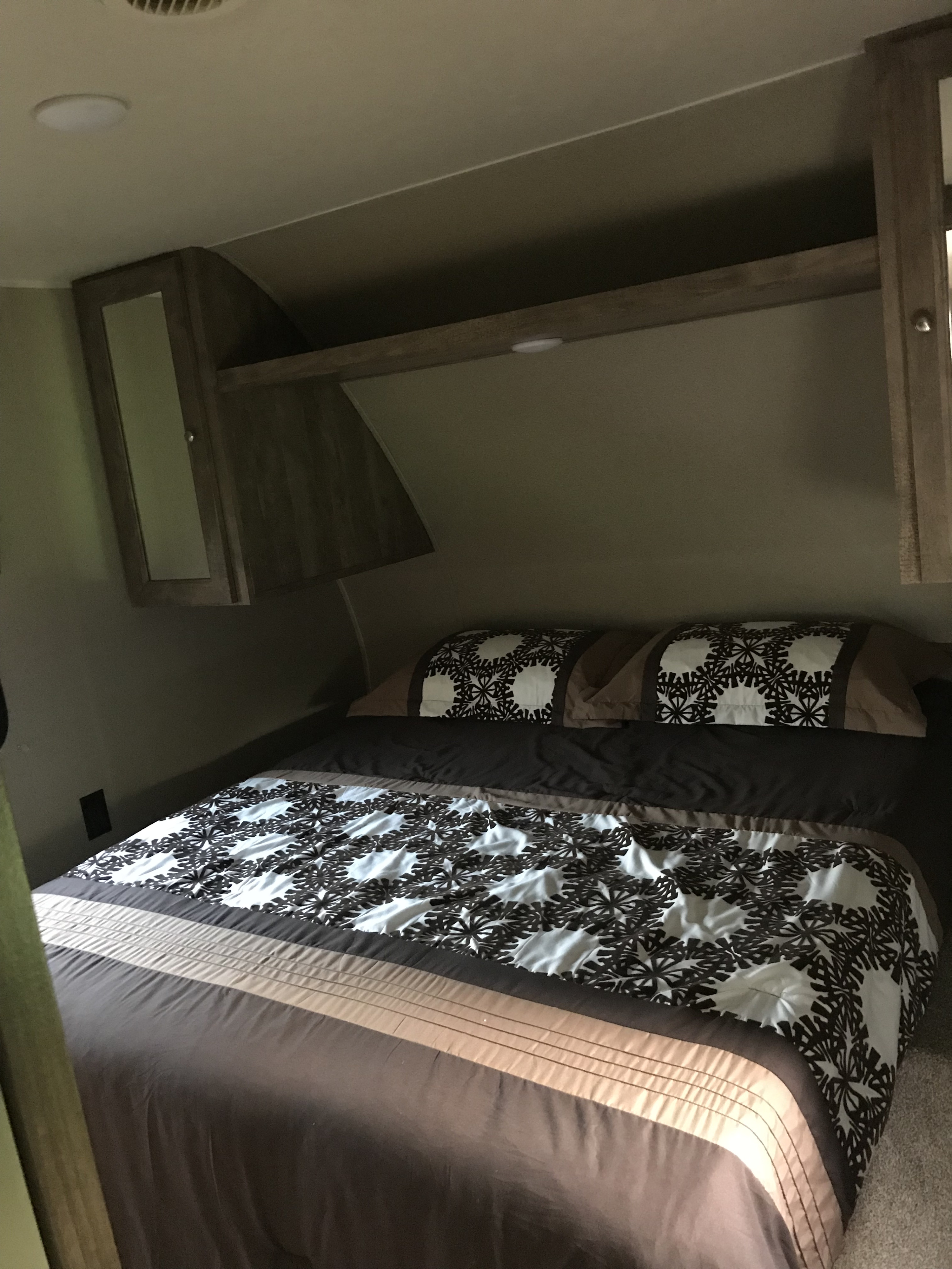 Cozy RV rental bedroom featuring a patterned bed, overhead storage, and integrated lighting, ideal for comfortable travel.. Forest River Puma 2018