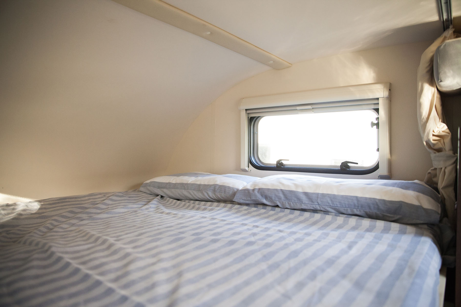 A cozy RV rental interior: a bed with blue & white striped linens, a bright window for natural light.. Roller Team Zefrio 675 2020