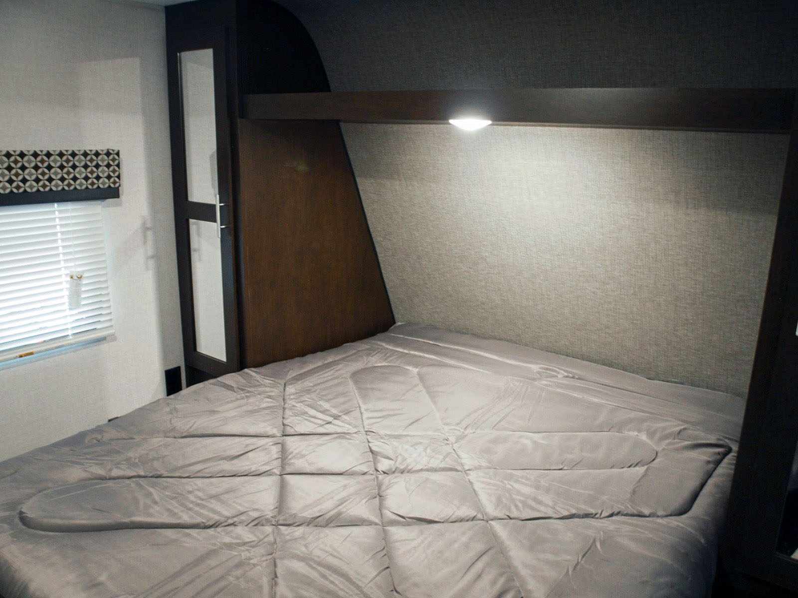 Inside an RV rental: a compact bedroom with a gray bed, window with blinds, and mirrored wardrobe. Ready for travel.. K-Z Manufacturing Sportsman Classic 2019