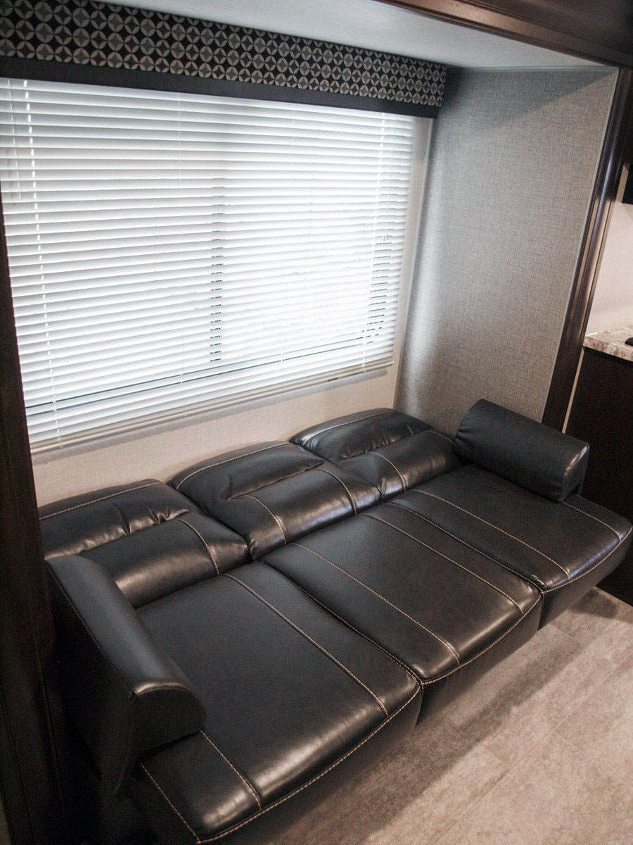 RV rental interior features a versatile dark leather sofa/bed near a window with blinds, offering cozy space.. K-Z Manufacturing Sportsman Classic 2019