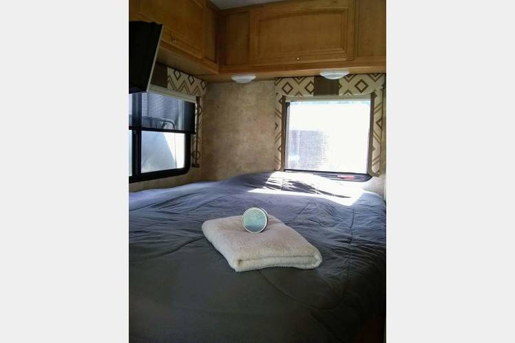 Inside an RV rental: a neat bedroom with a comfy bed, windows, and overhead cabinets, perfect for travel.. Winnebago Access 2015