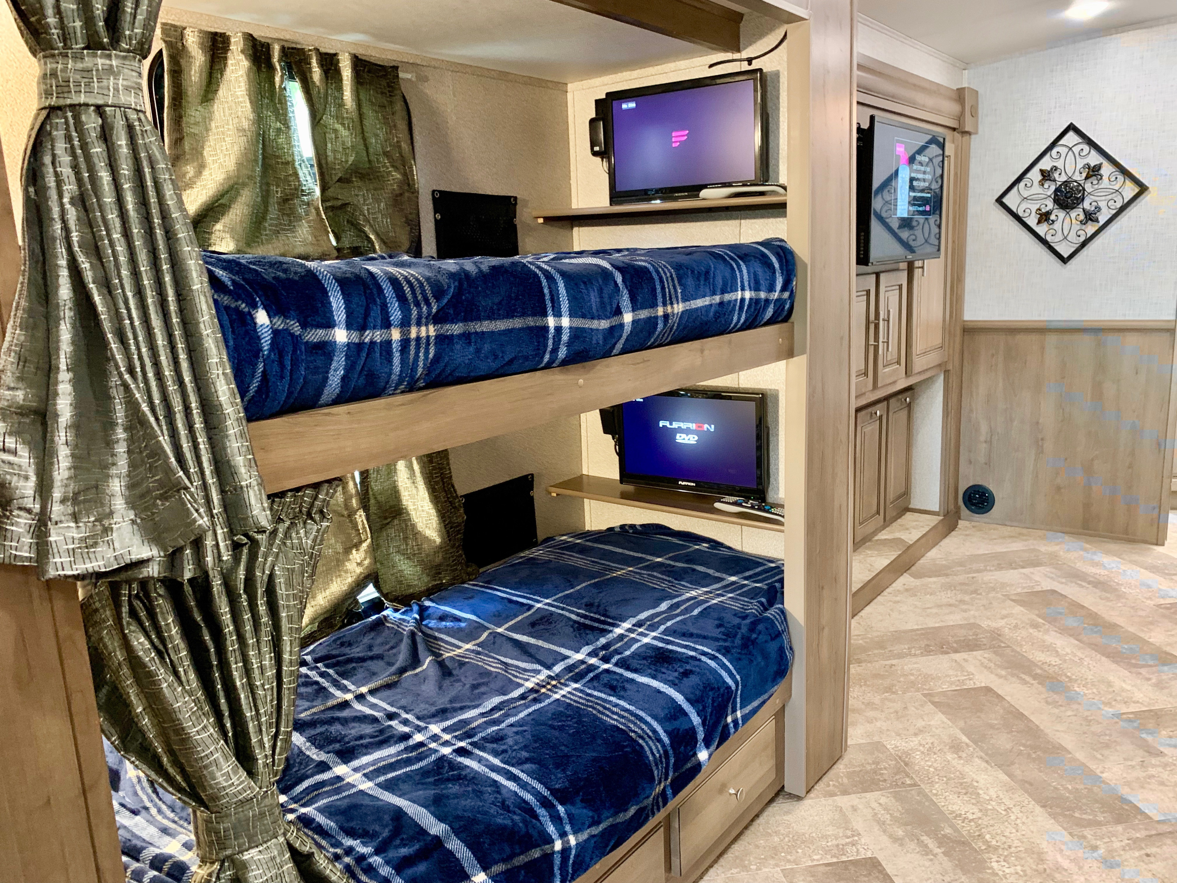 Inside this **rv rental**, two bunk beds with blue plaid blankets and individual TVs offer comfort and entertainment in a compact design.. Forest River Georgetown 2019