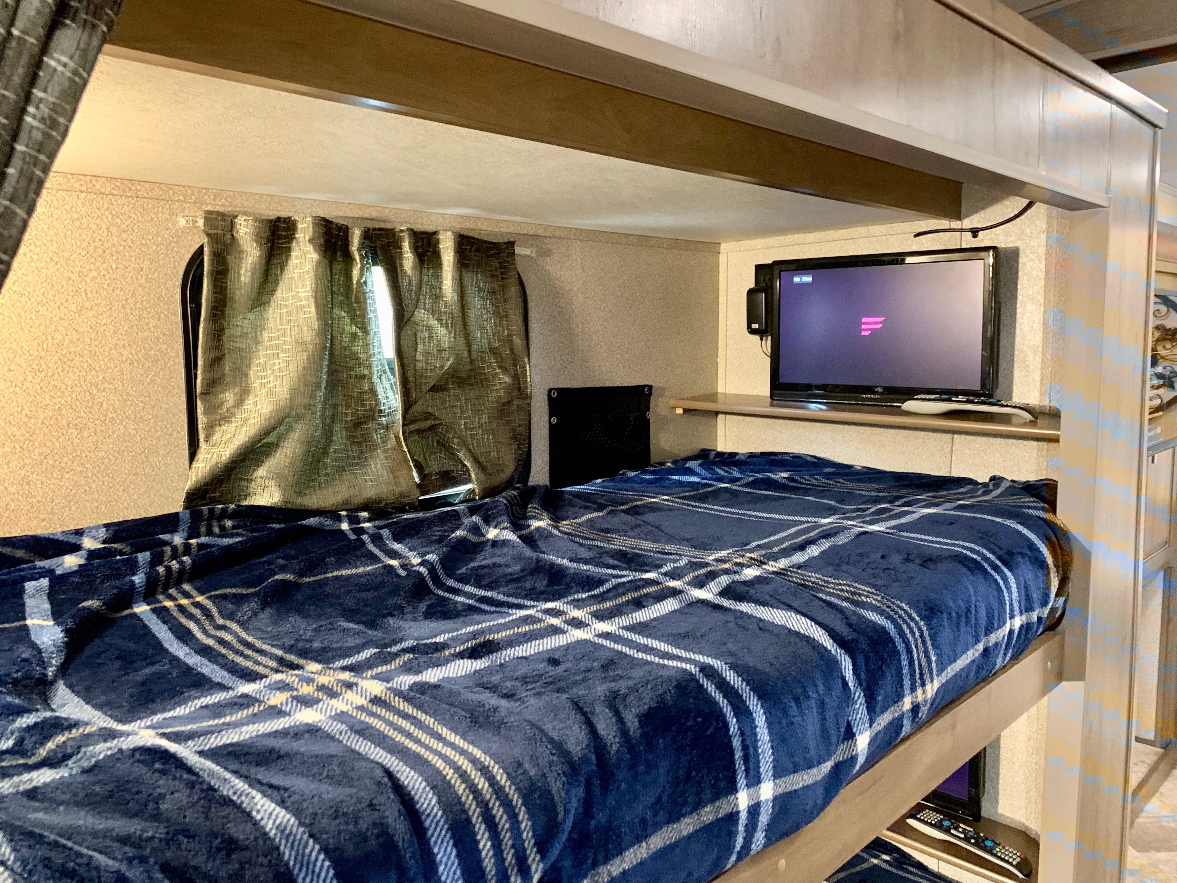 Cozy RV rental bunk bed with TV for comfortable travel. Blue plaid blanket & window curtains.. Forest River Georgetown 2019