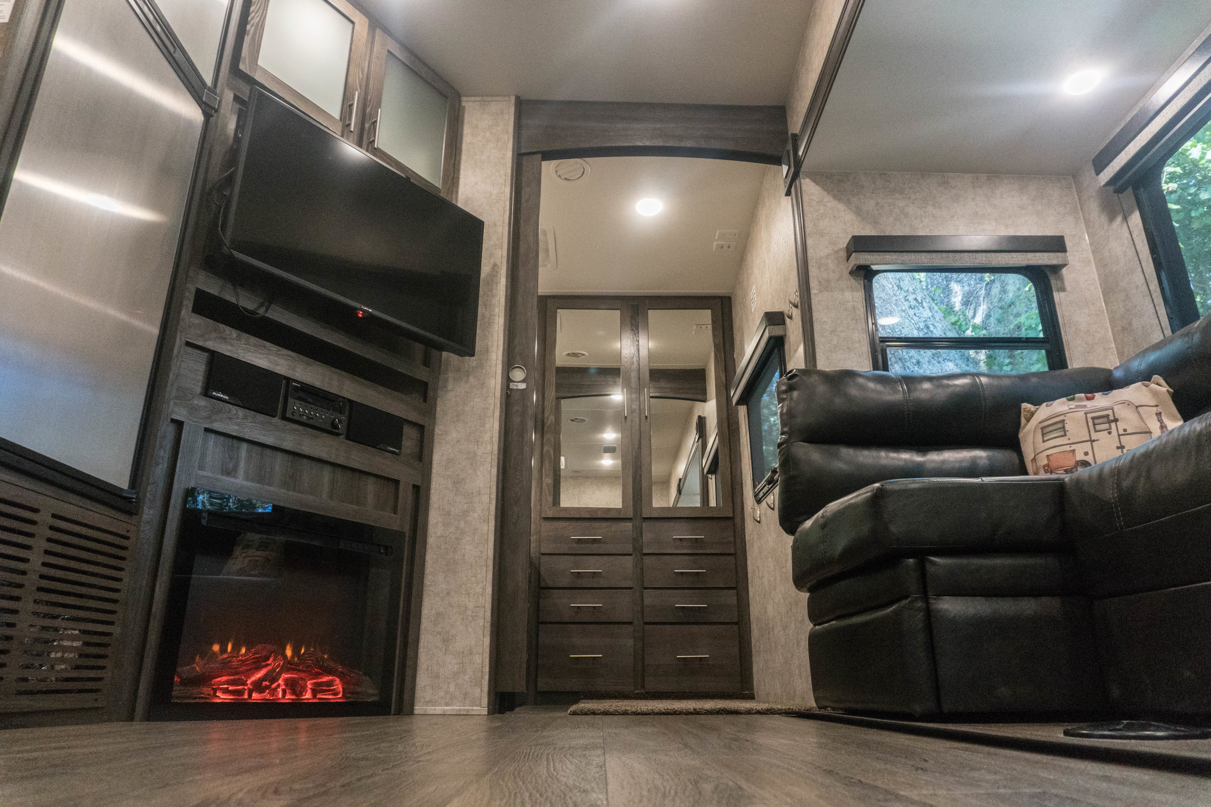 Modern RV rental interior: living area with TV, fireplace, and sofa; plus fridge and mirrored storage.. Open Range Light 2018